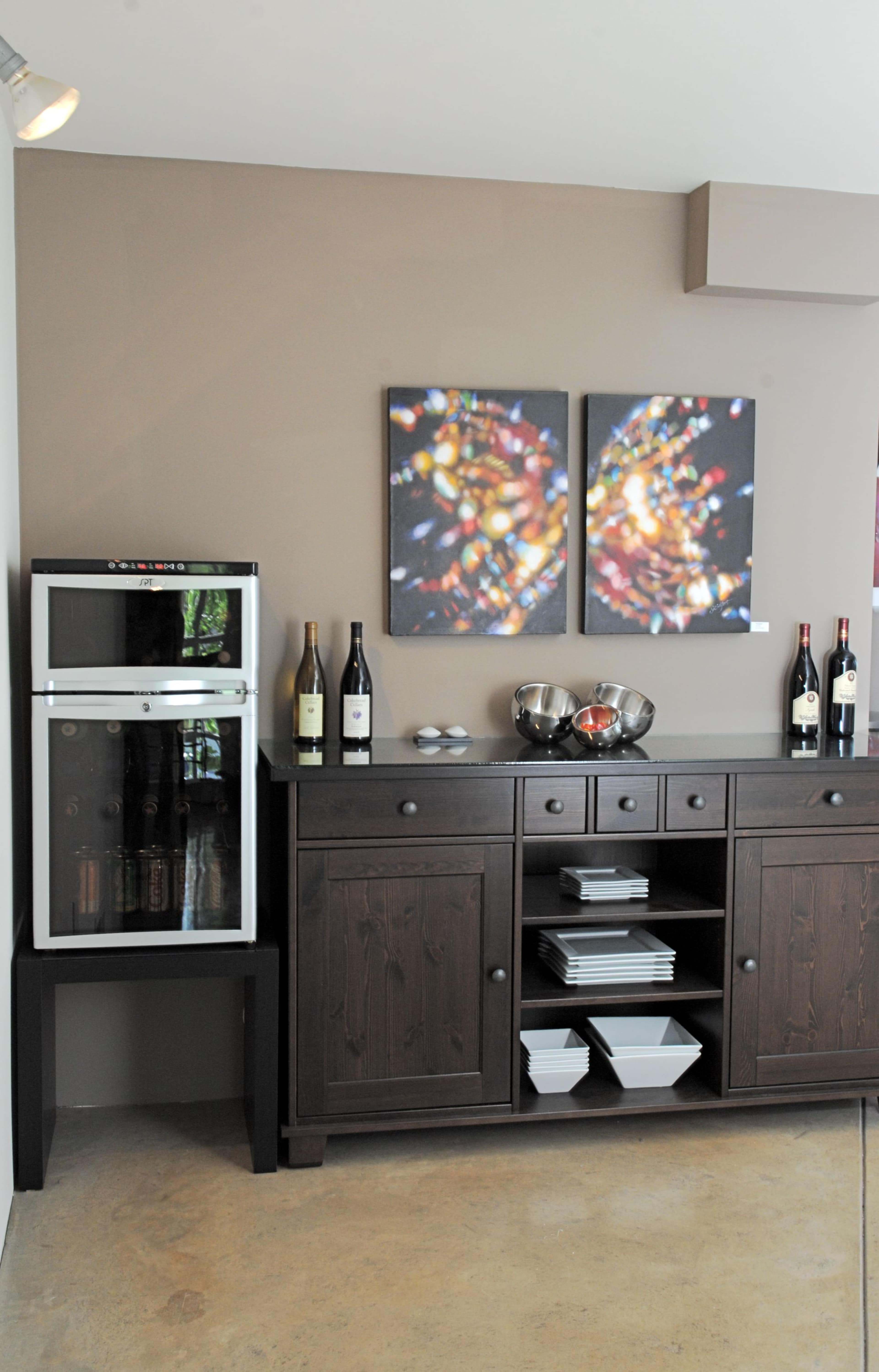 A modern interior featuring a wine fridge next to a wooden sideboard with bottles of wine and decorative items.