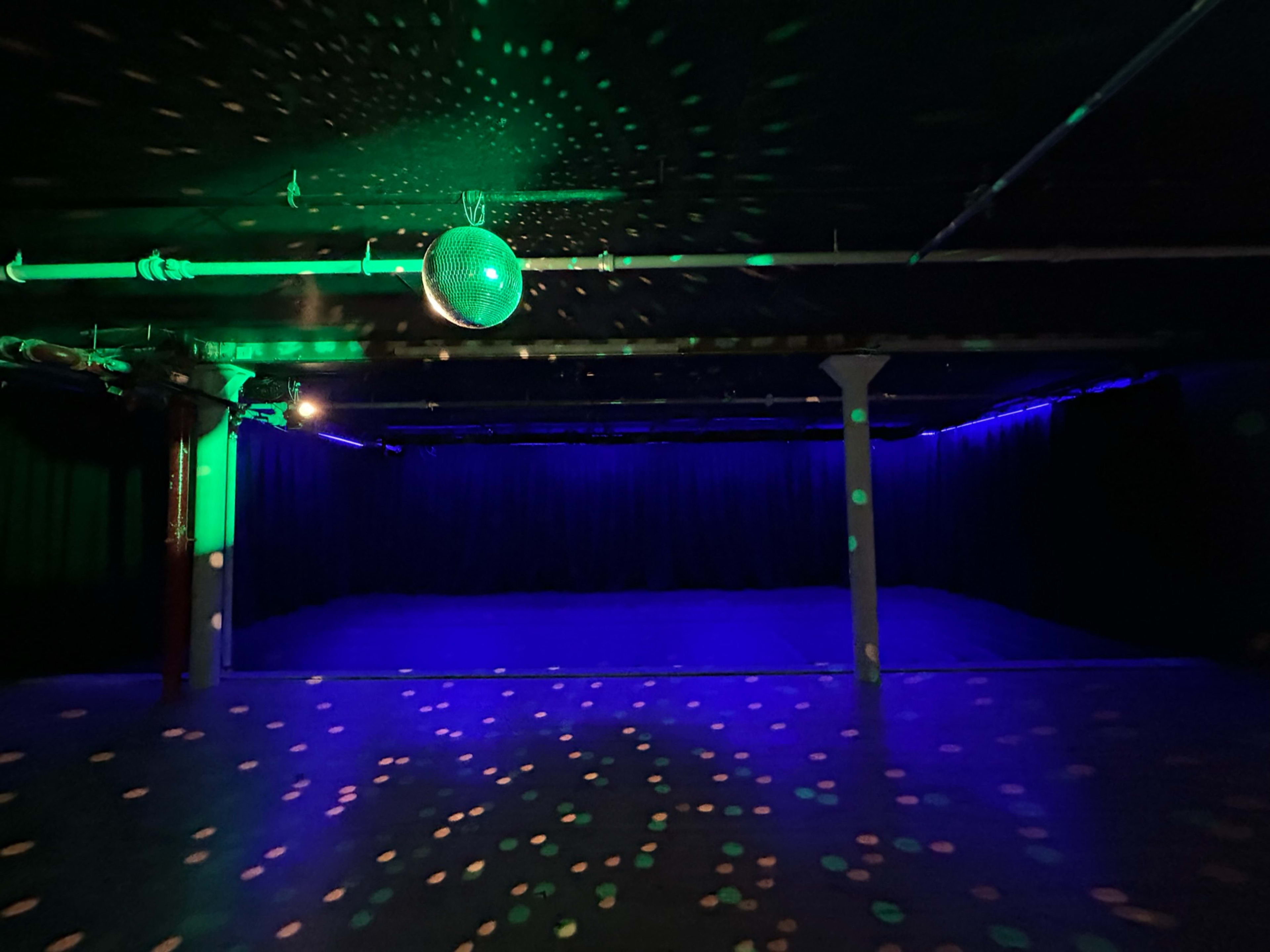 A dimly lit dance floor with colorful lights and a disco ball hanging from the ceiling.