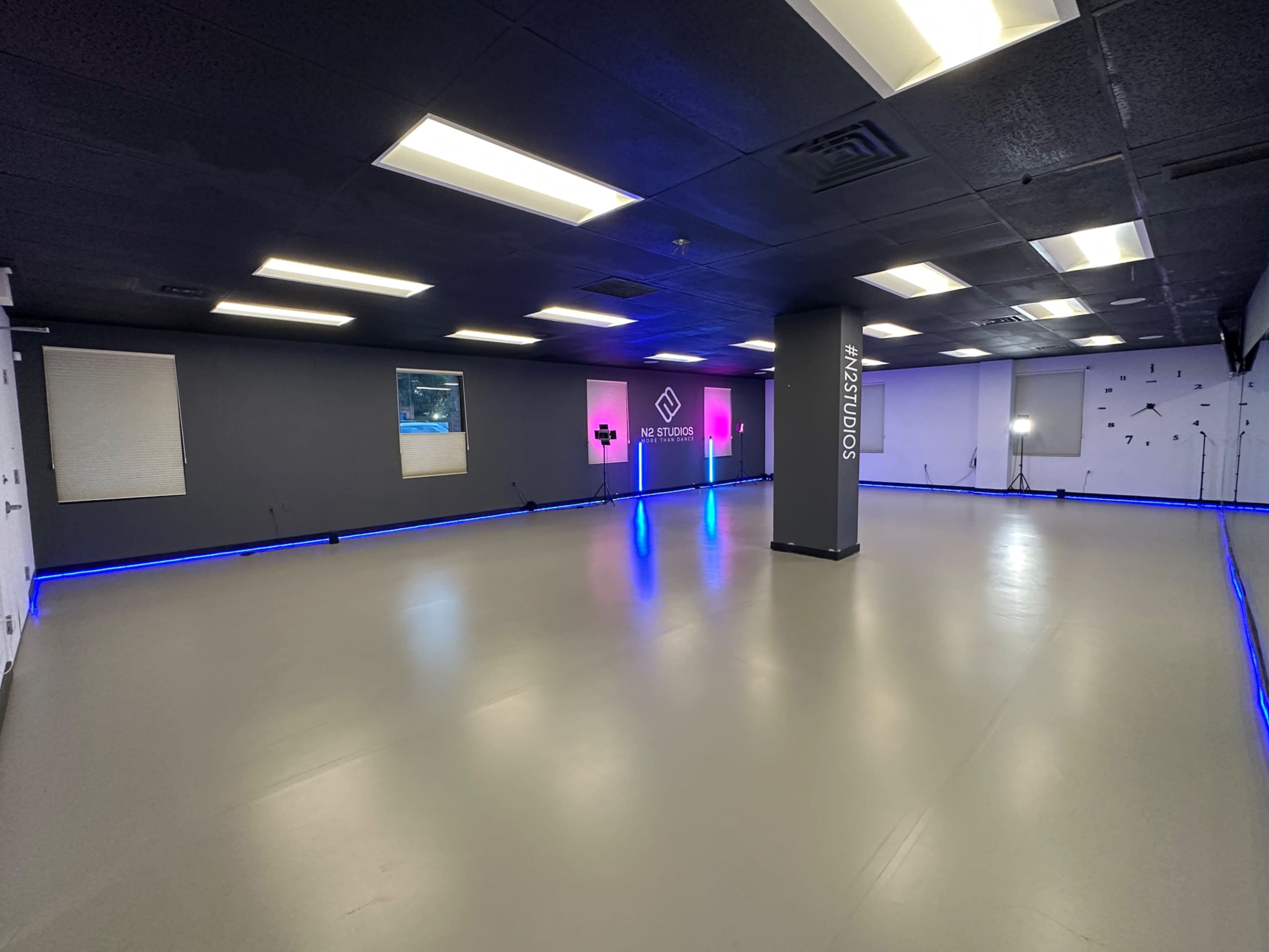 A spacious, brightly lit studio with a smooth gray floor, featuring blue LED lights along the perimeter and a central column displaying the name "H4Z8T0S."