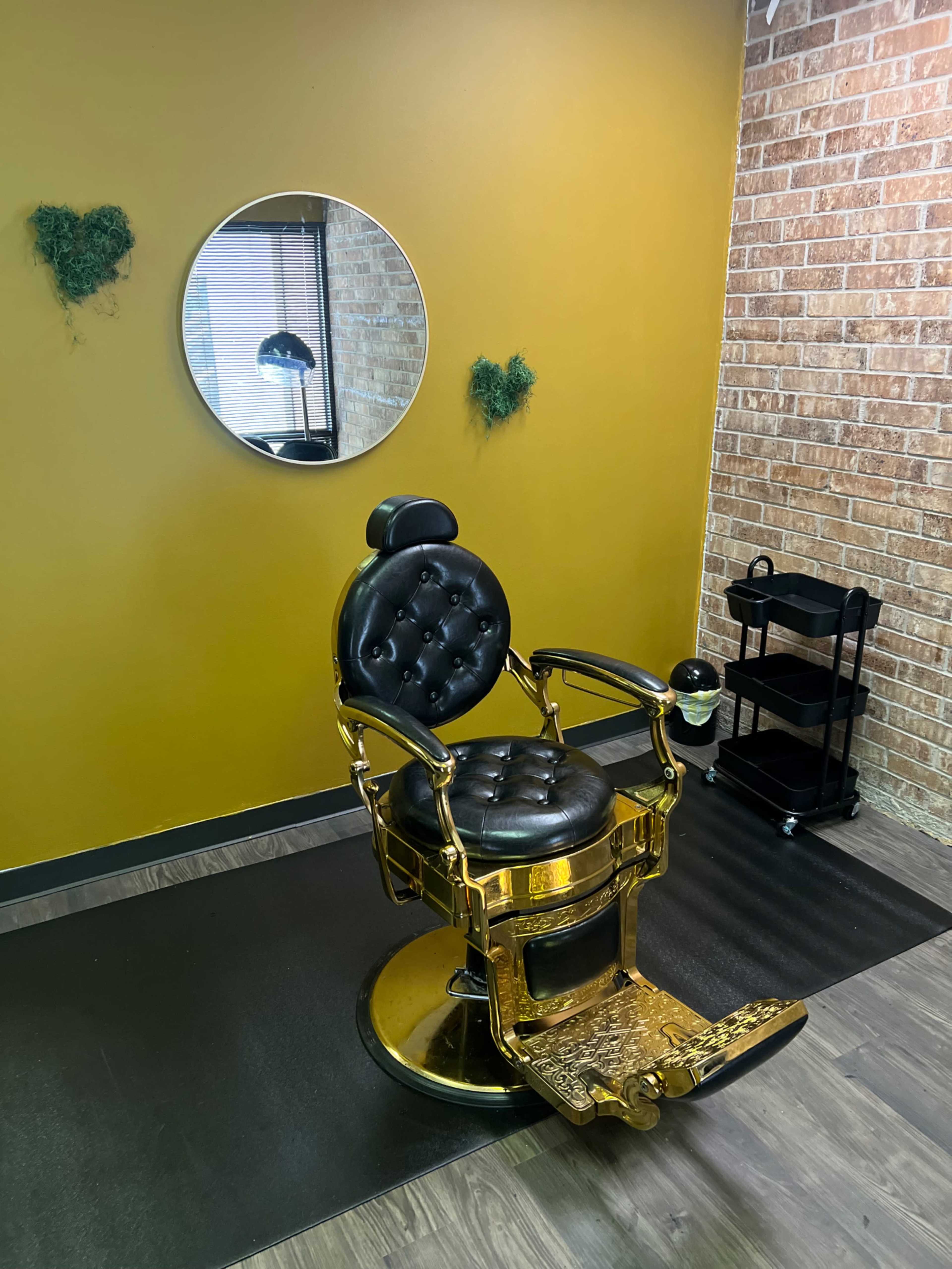 The image shows a vintage barber chair in a salon, positioned in front of a round mirror on a mustard-colored wall.