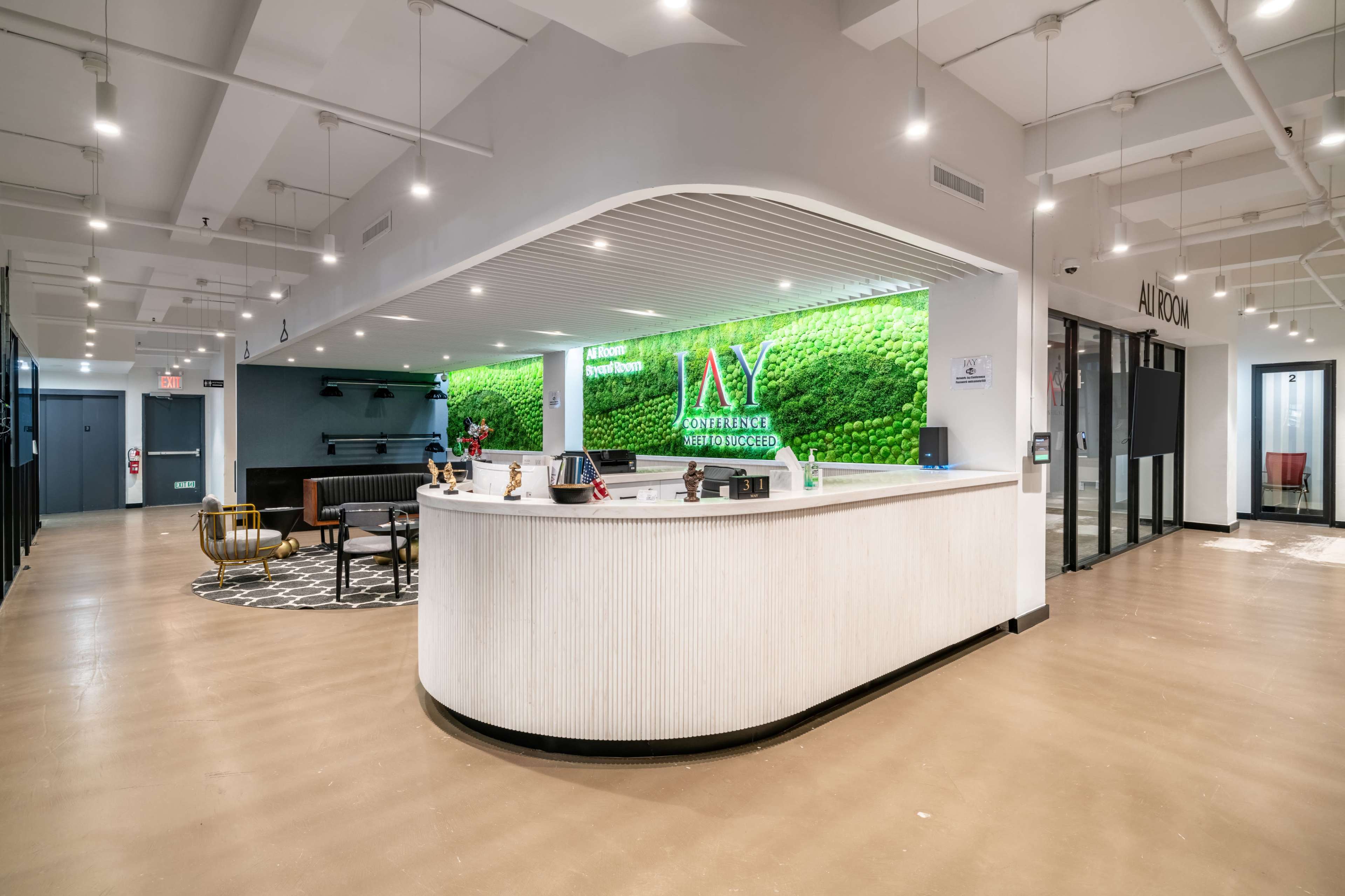 The image shows a modern reception area with a curved front desk, a green moss wall feature, and various seating arrangements in an open space.