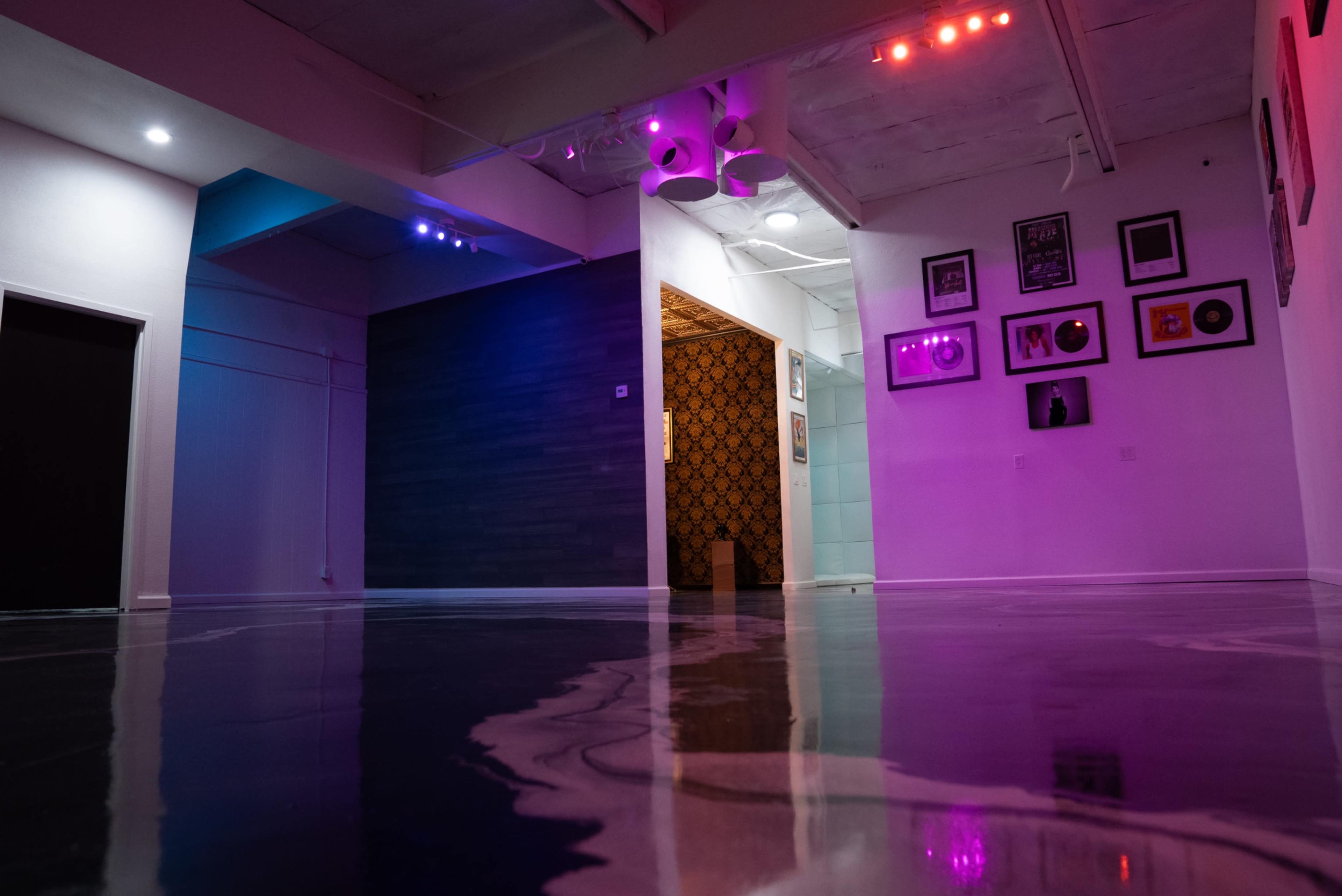 A spacious room with a glossy floor, featuring colorful lighting and a distinct wall with framed records and photos.