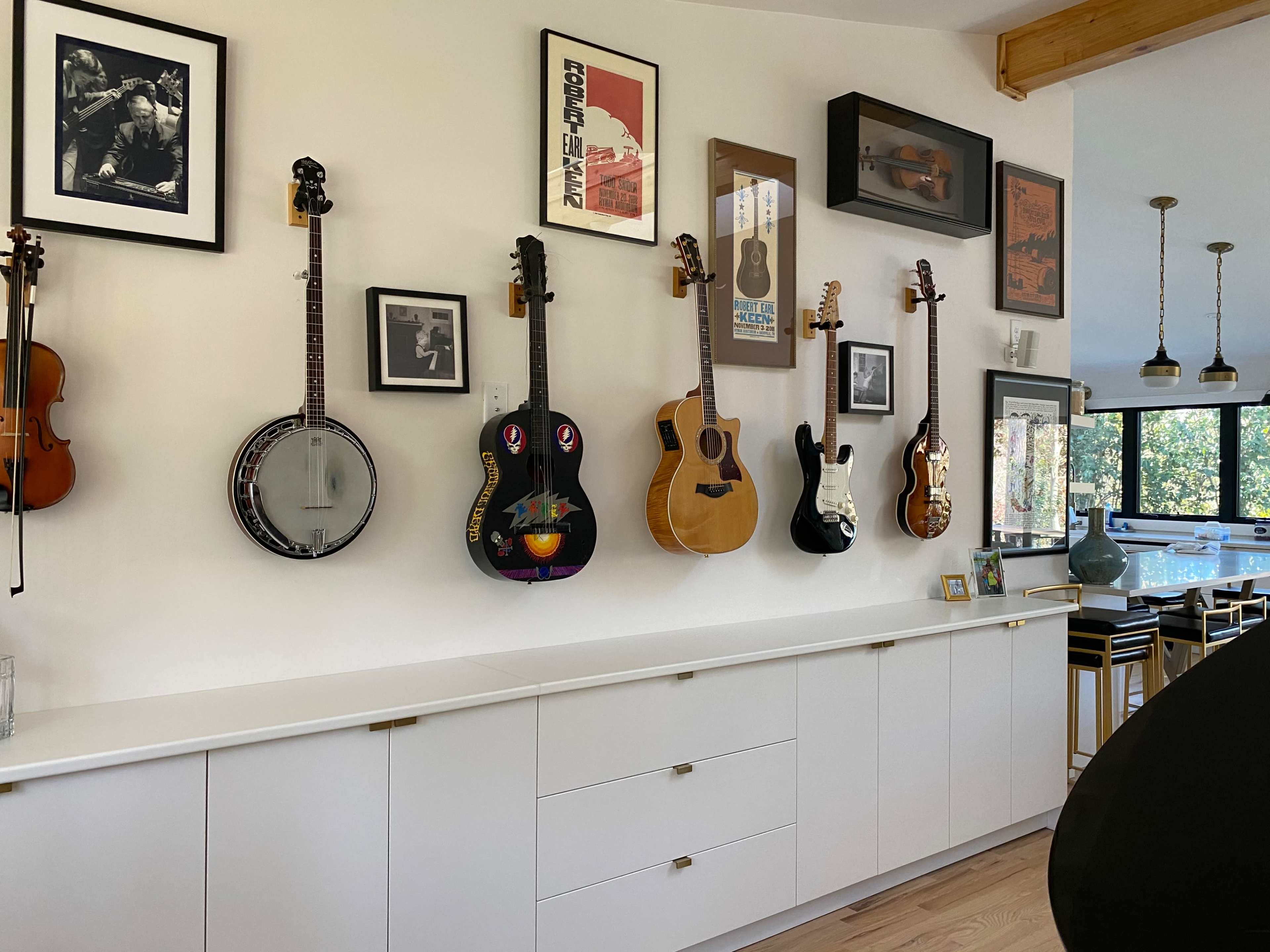 A white wall adorned with various musical instruments, including guitars, a banjo, and a violin, alongside framed photographs and artwork.