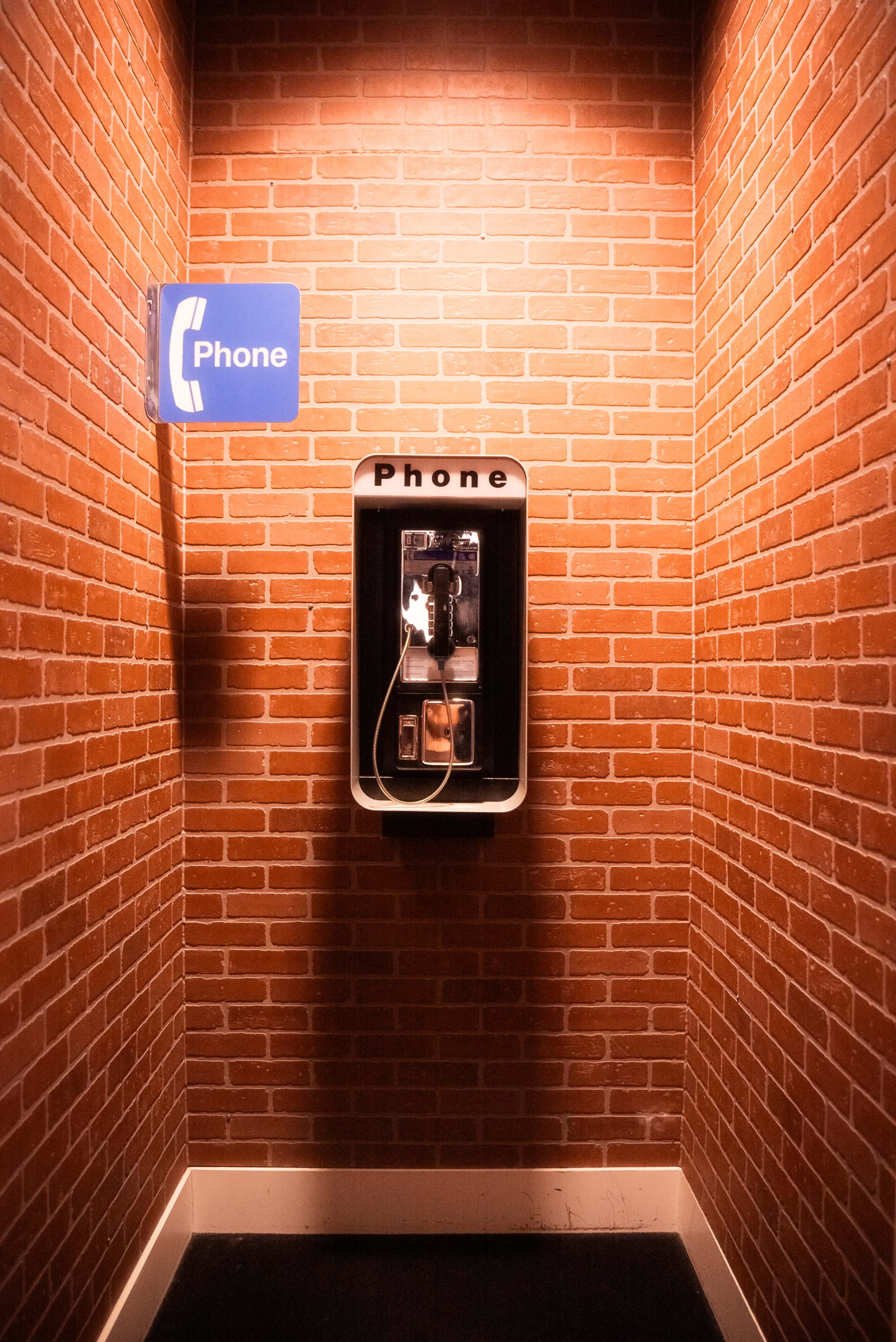 A payphone is mounted on a brick wall in a dimly lit hallway.