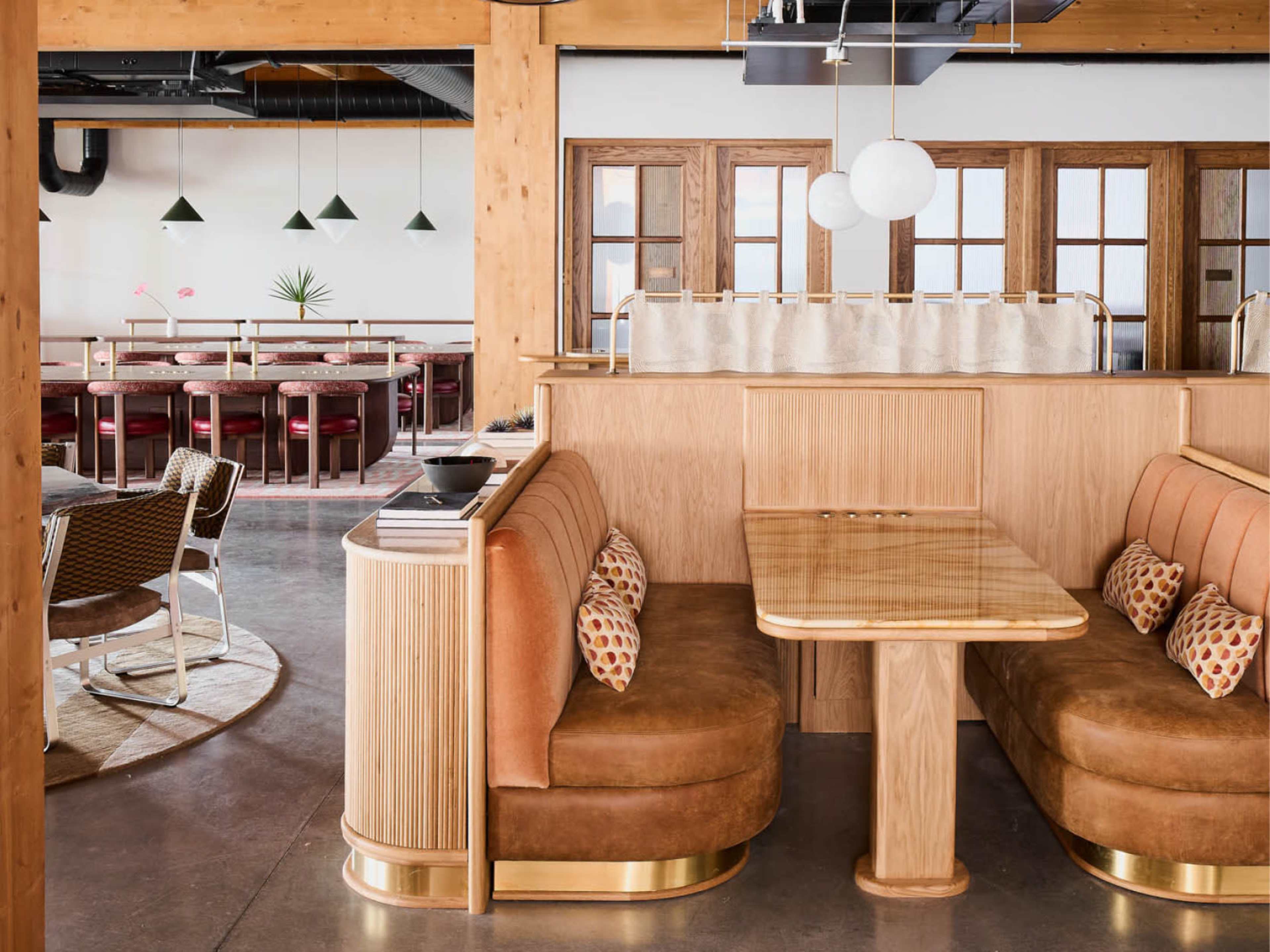 The image shows a contemporary restaurant interior featuring wooden accents, leather seating booths, and a seating area with round tables and chairs.