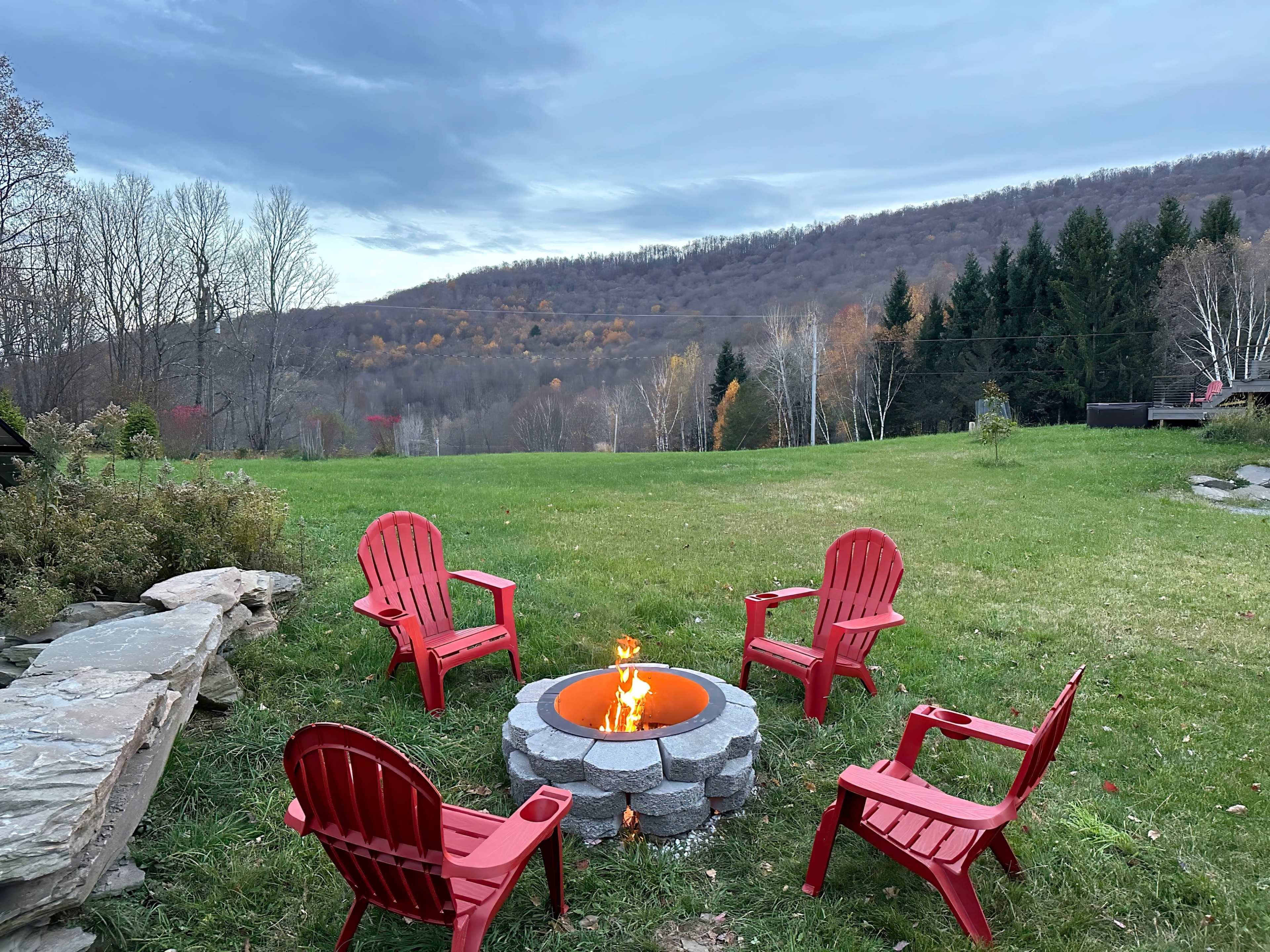 A circle of four red chairs surrounds a stone fire pit in a grassy field with a hillside in the background.