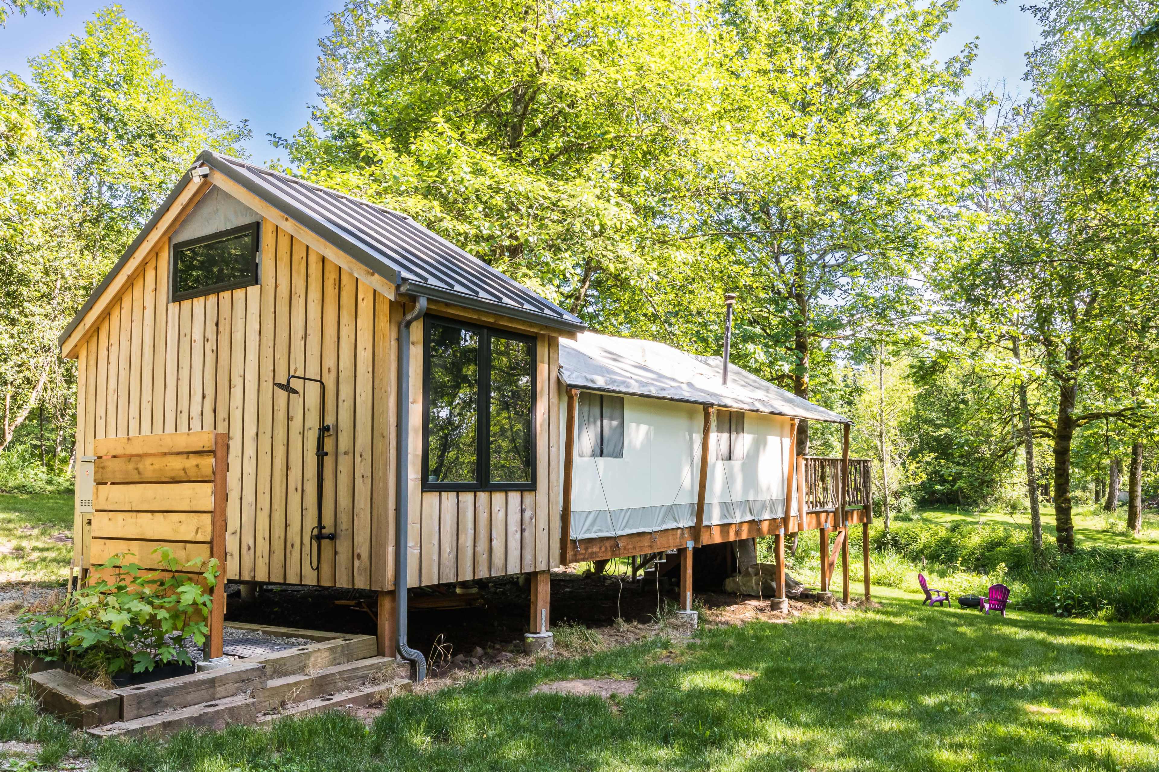 A wooden cabin with a metal roof and a deck is surrounded by trees and greenery.