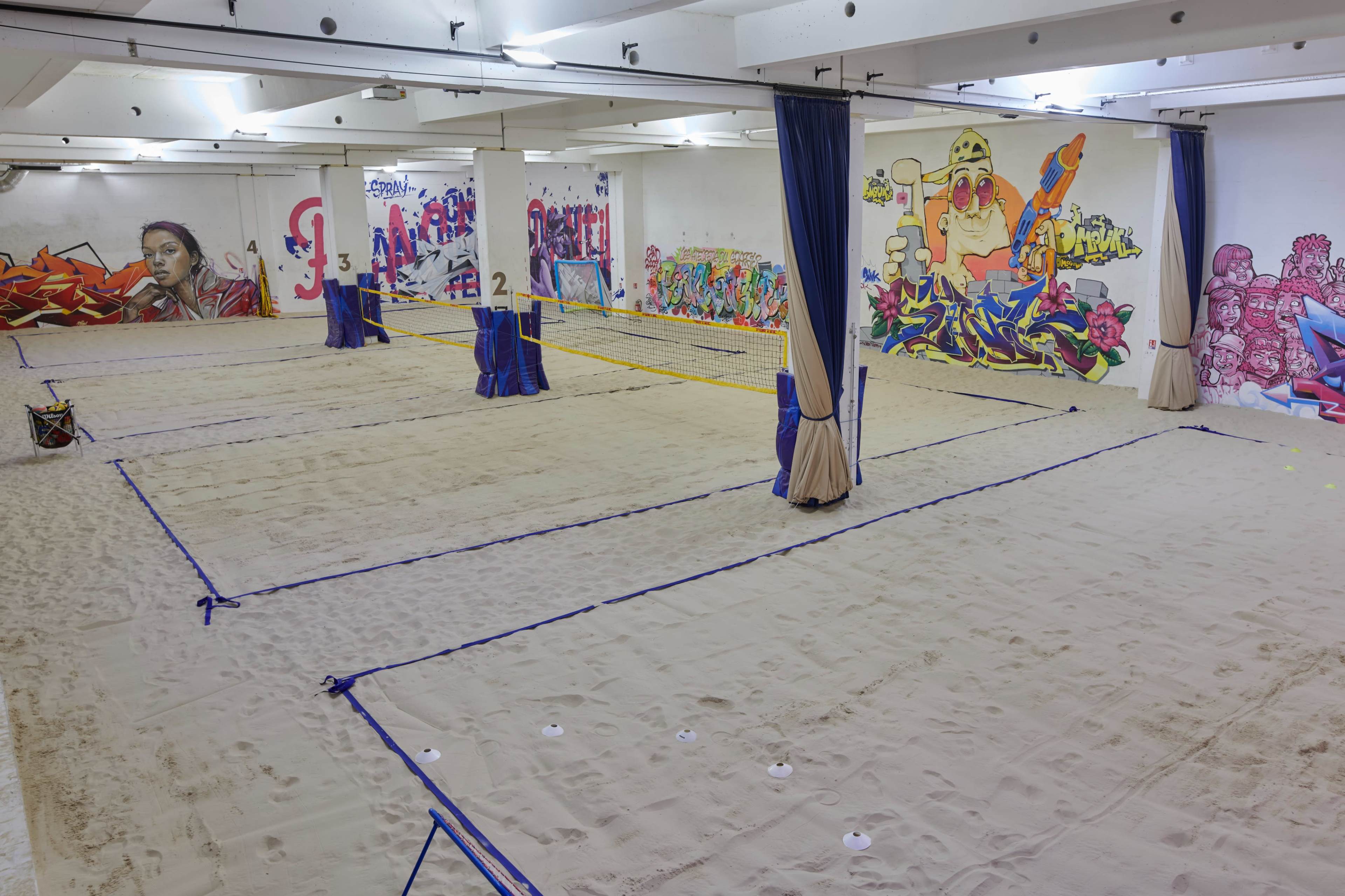 An indoor sand sports facility with multiple volleyball courts and colorful graffiti on the walls.