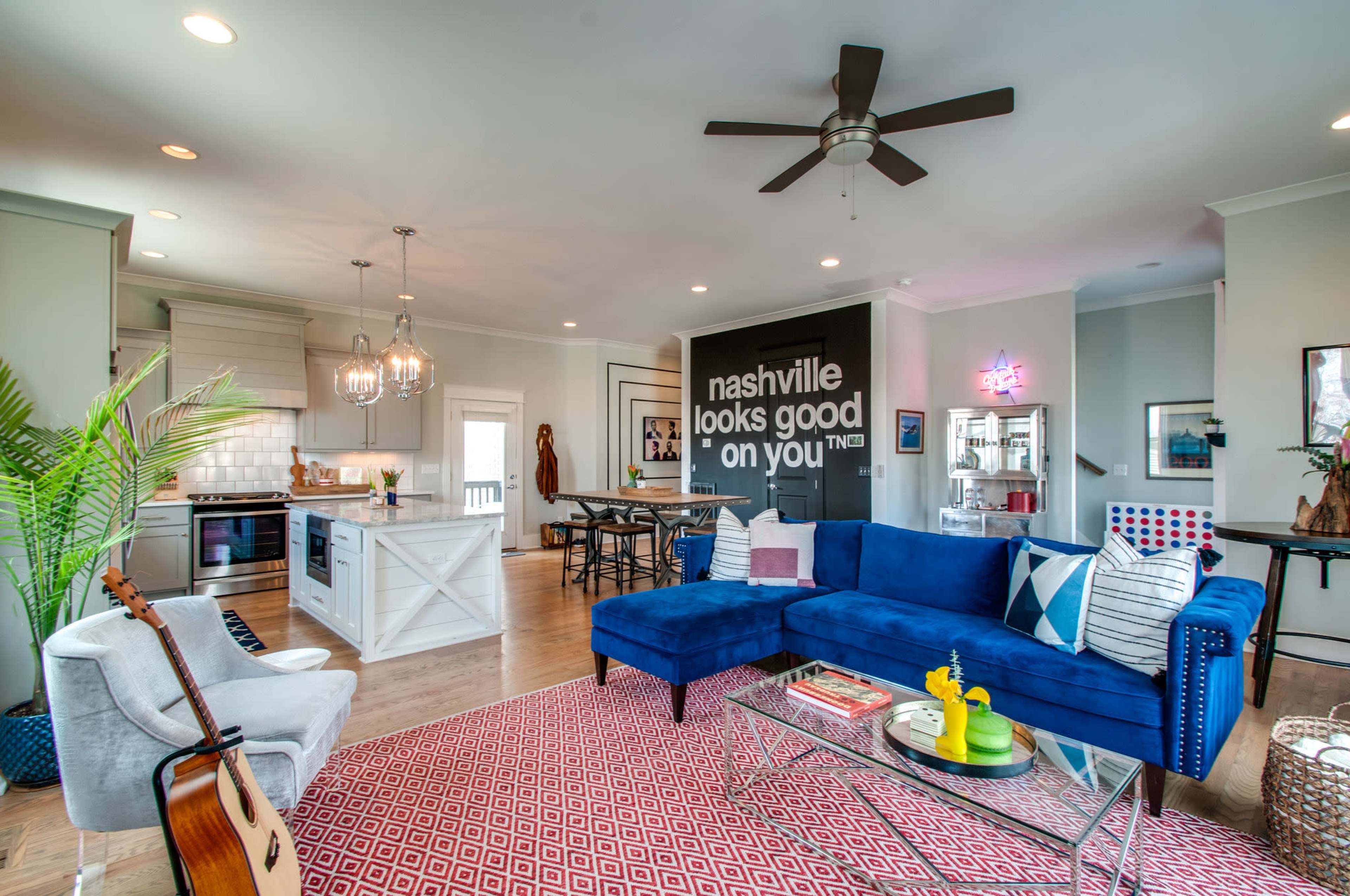 A modern living space featuring a blue sectional sofa, a dining area with a black table, and a kitchen with white cabinetry.