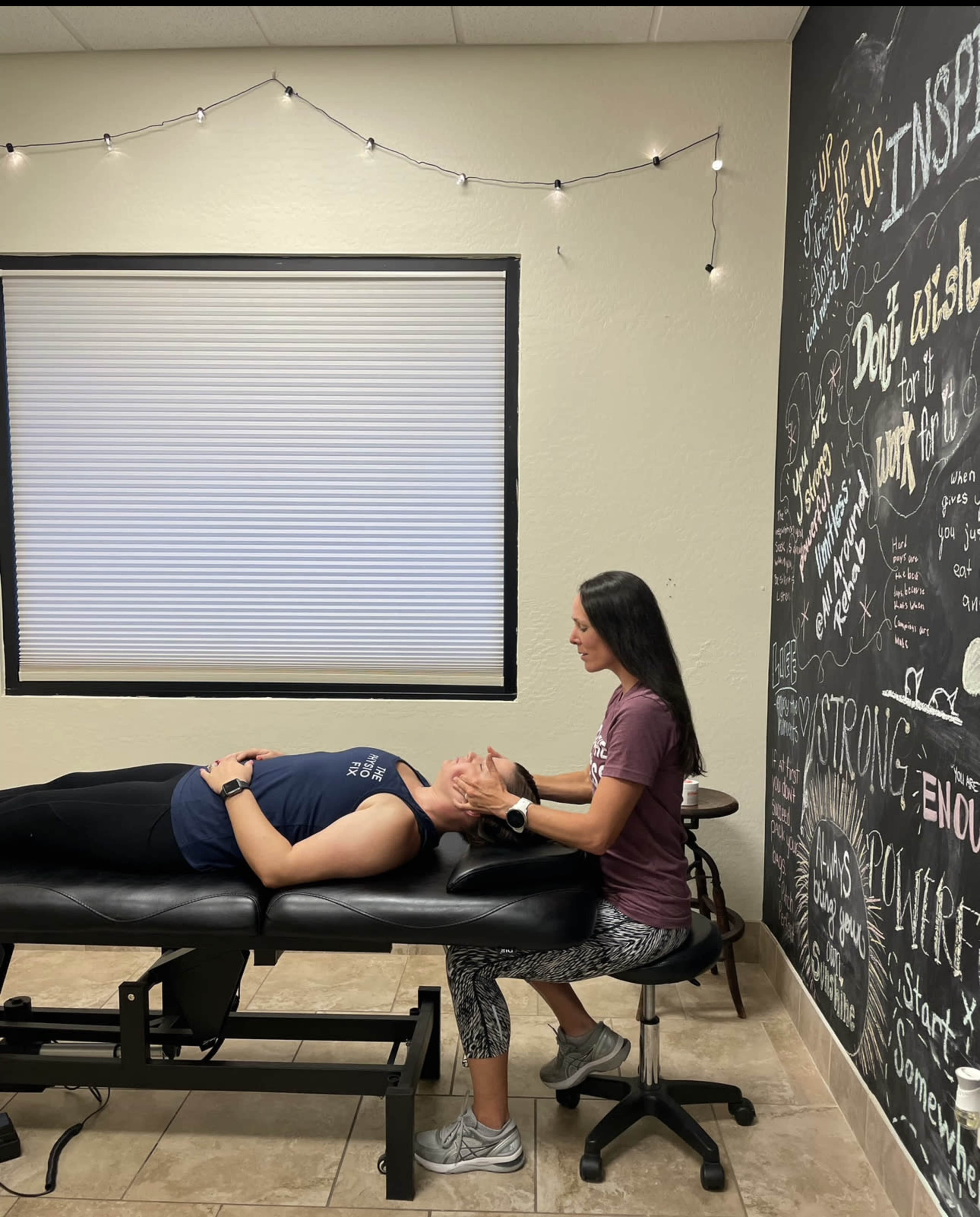 A person is receiving a therapeutic treatment while lying on a massage table in a room with motivational quotes on the wall.