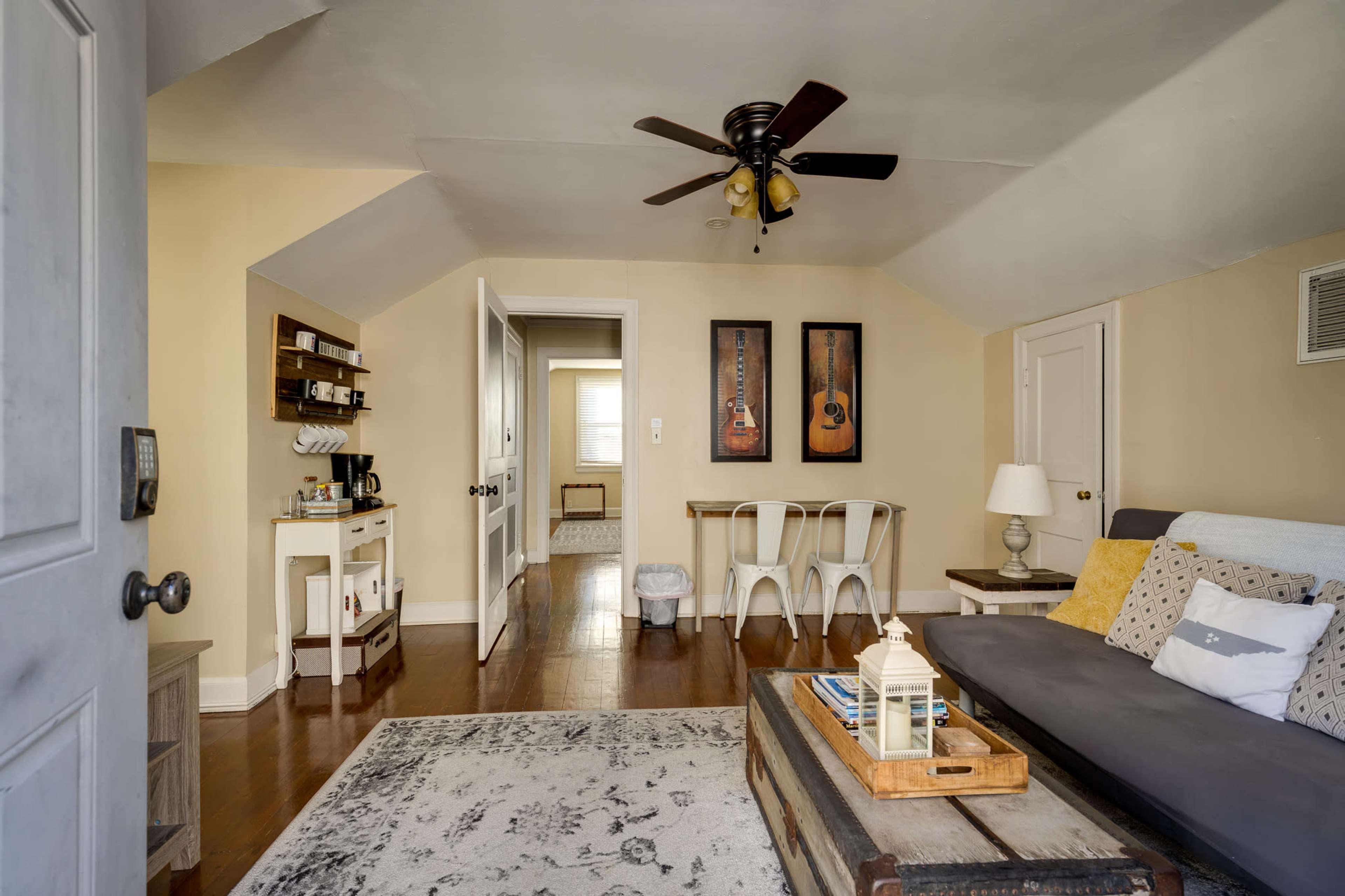 The image shows a cozy living space with a gray couch, a wooden coffee table, and a dining area featuring a table and chairs, all set under a ceiling fan.
