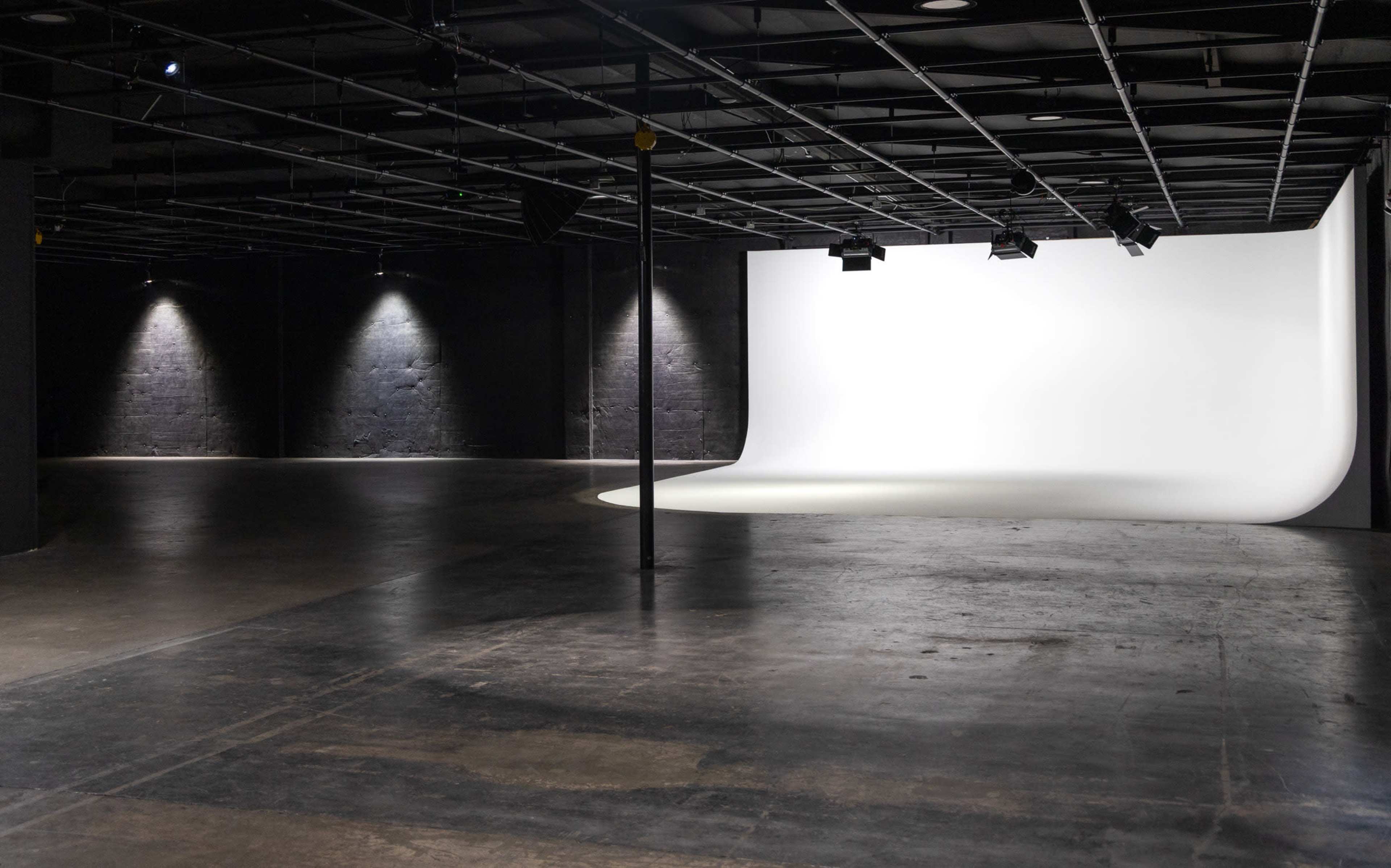 The image shows a spacious studio with a curved white backdrop and dim lighting against dark gray walls.