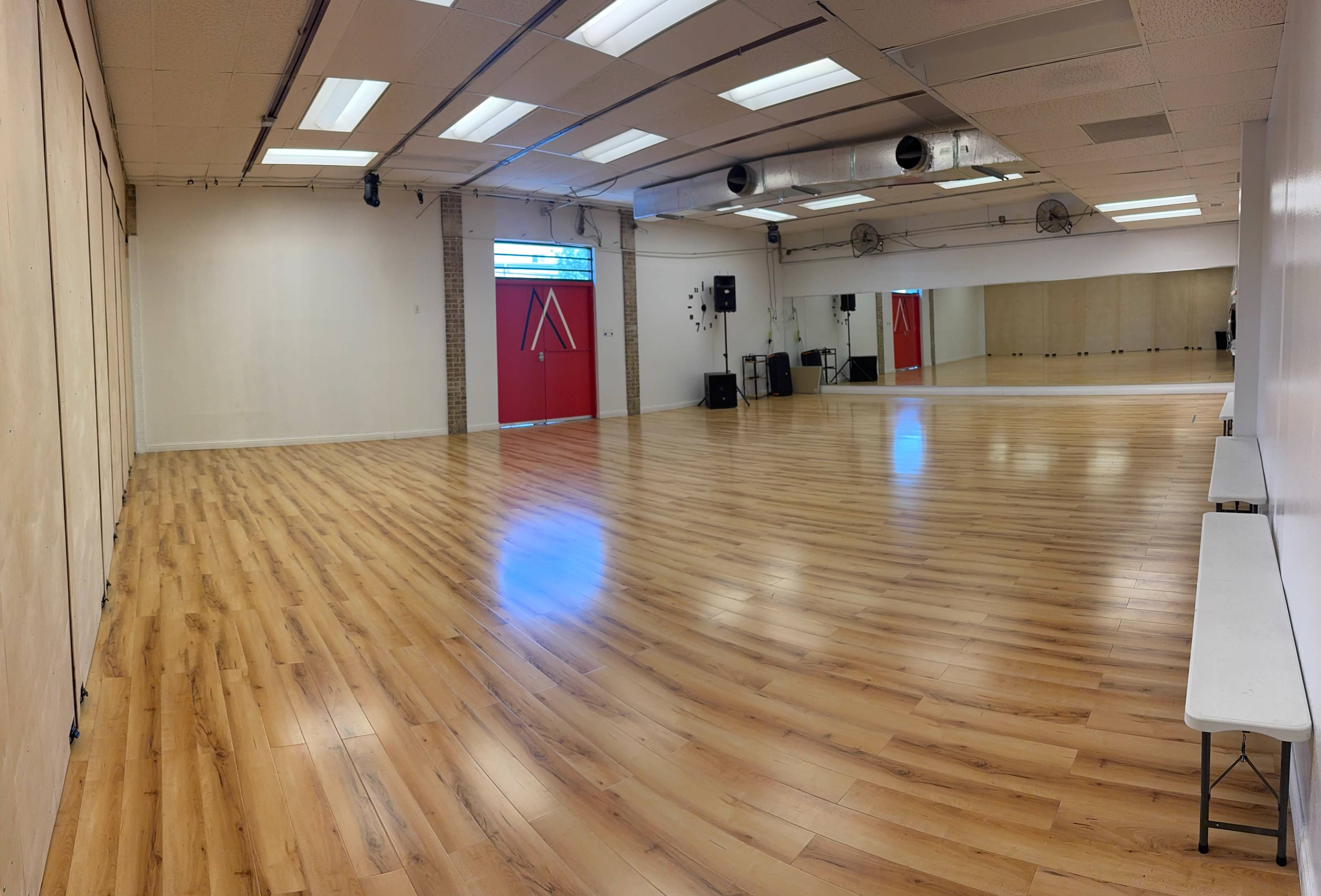 The image shows a spacious dance studio with wooden flooring, large mirrors on one wall, and red curtains at the far end.