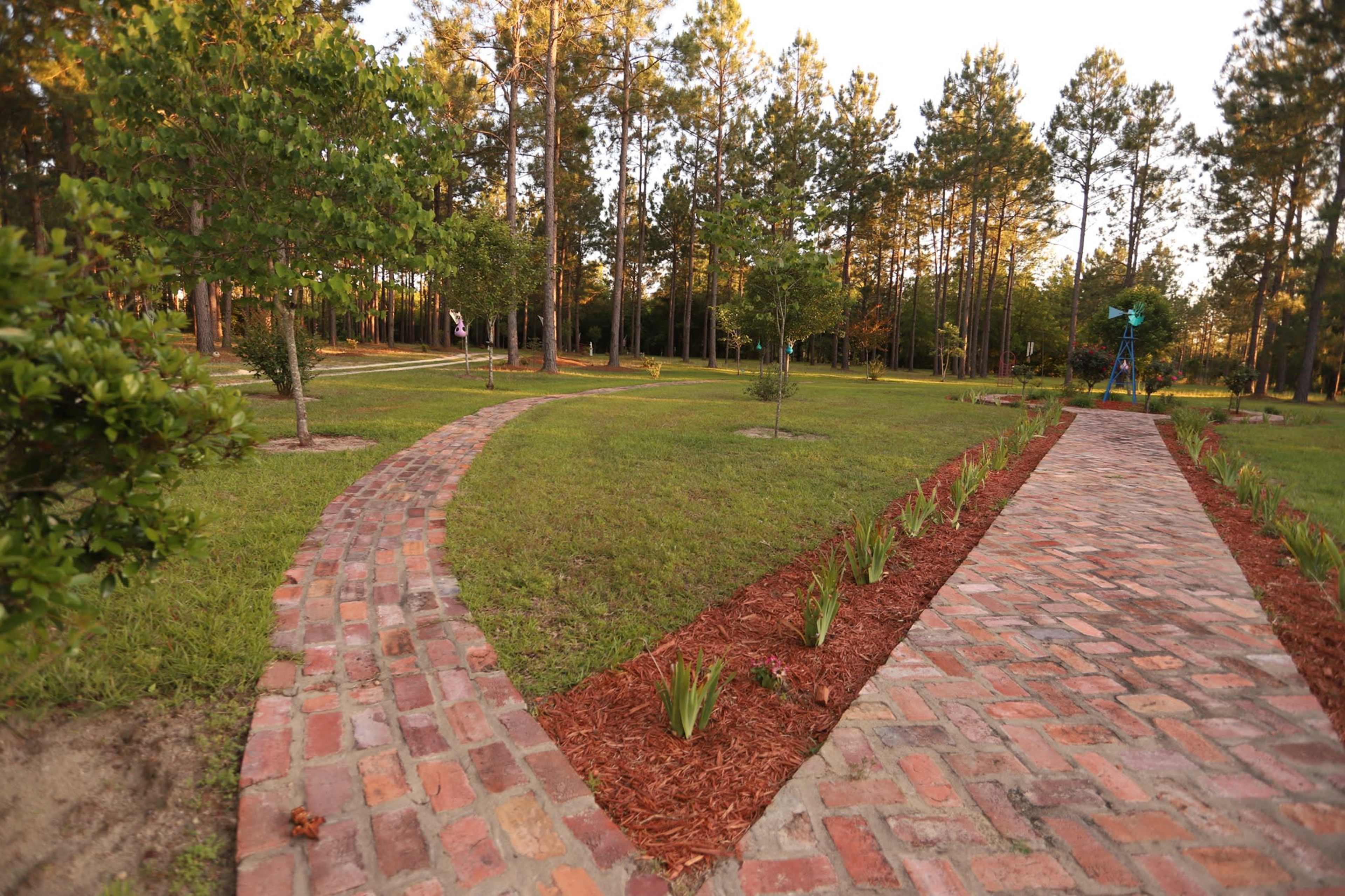 The image shows a landscaped area with winding brick pathways surrounded by greenery and trees.