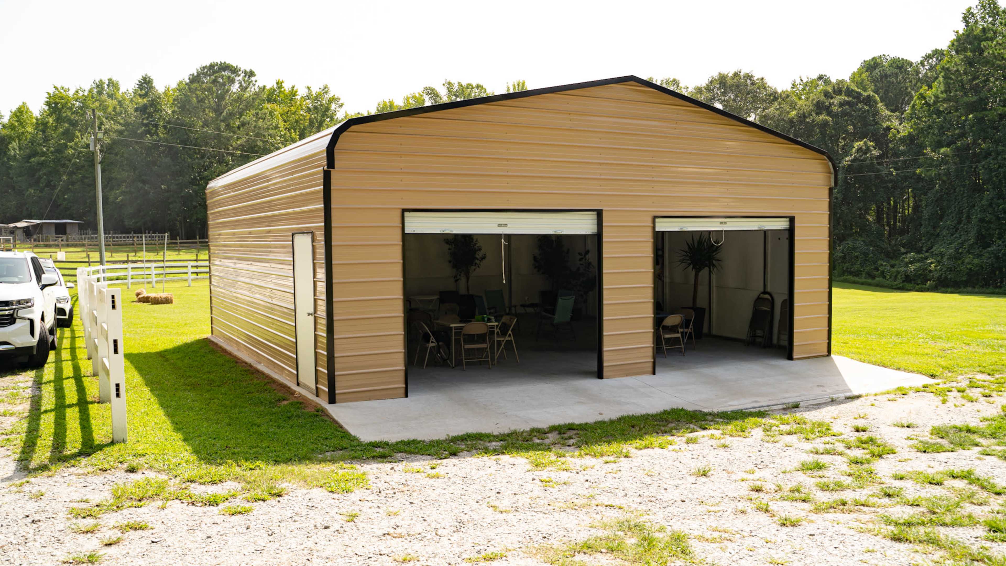 A large metal building with roll-up doors on two sides, situated on a grassy area beside a gravel path.