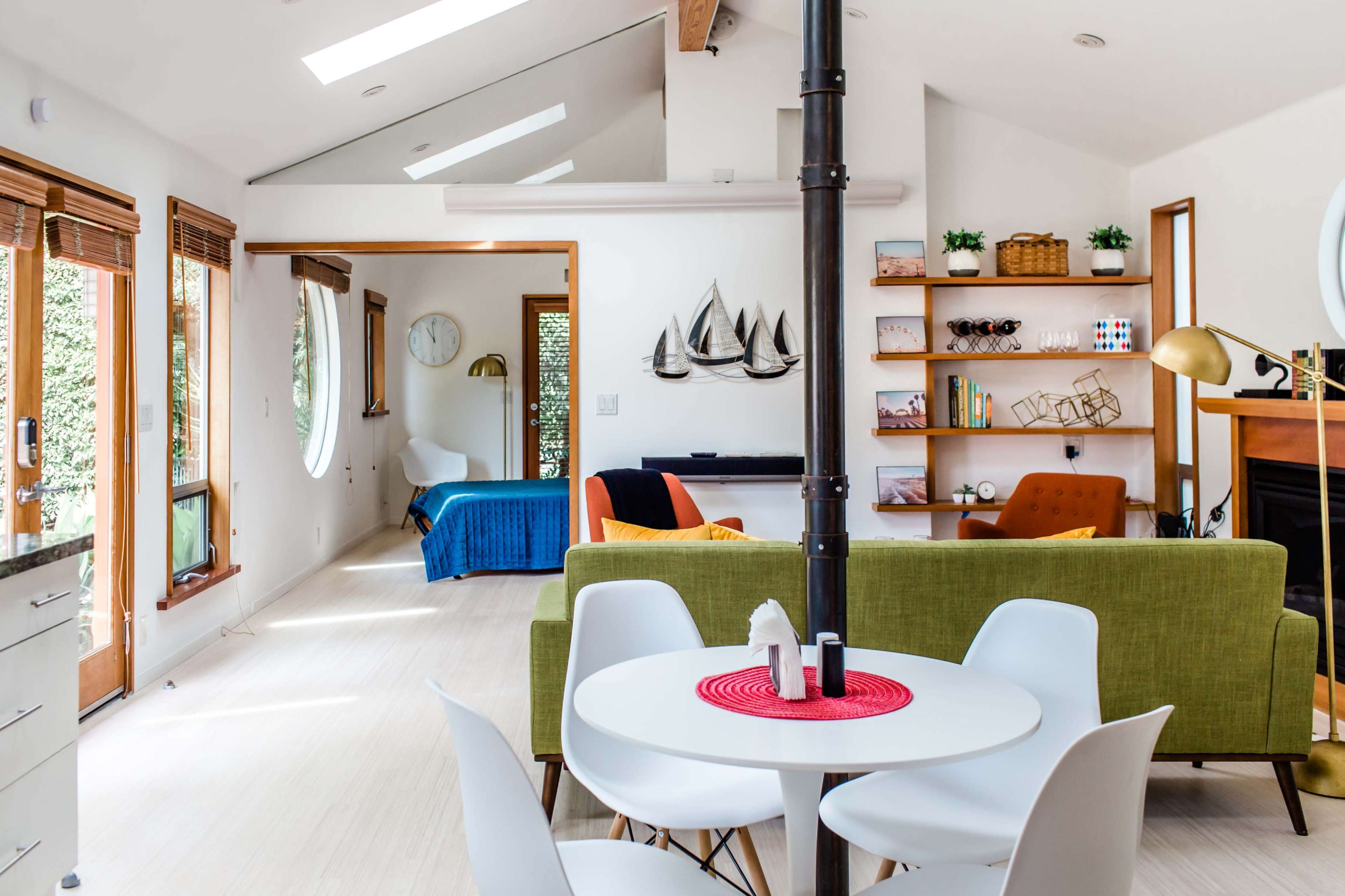 A modern living space features a circular window, a green sofa, a white dining table, and a separate room visible in the background.