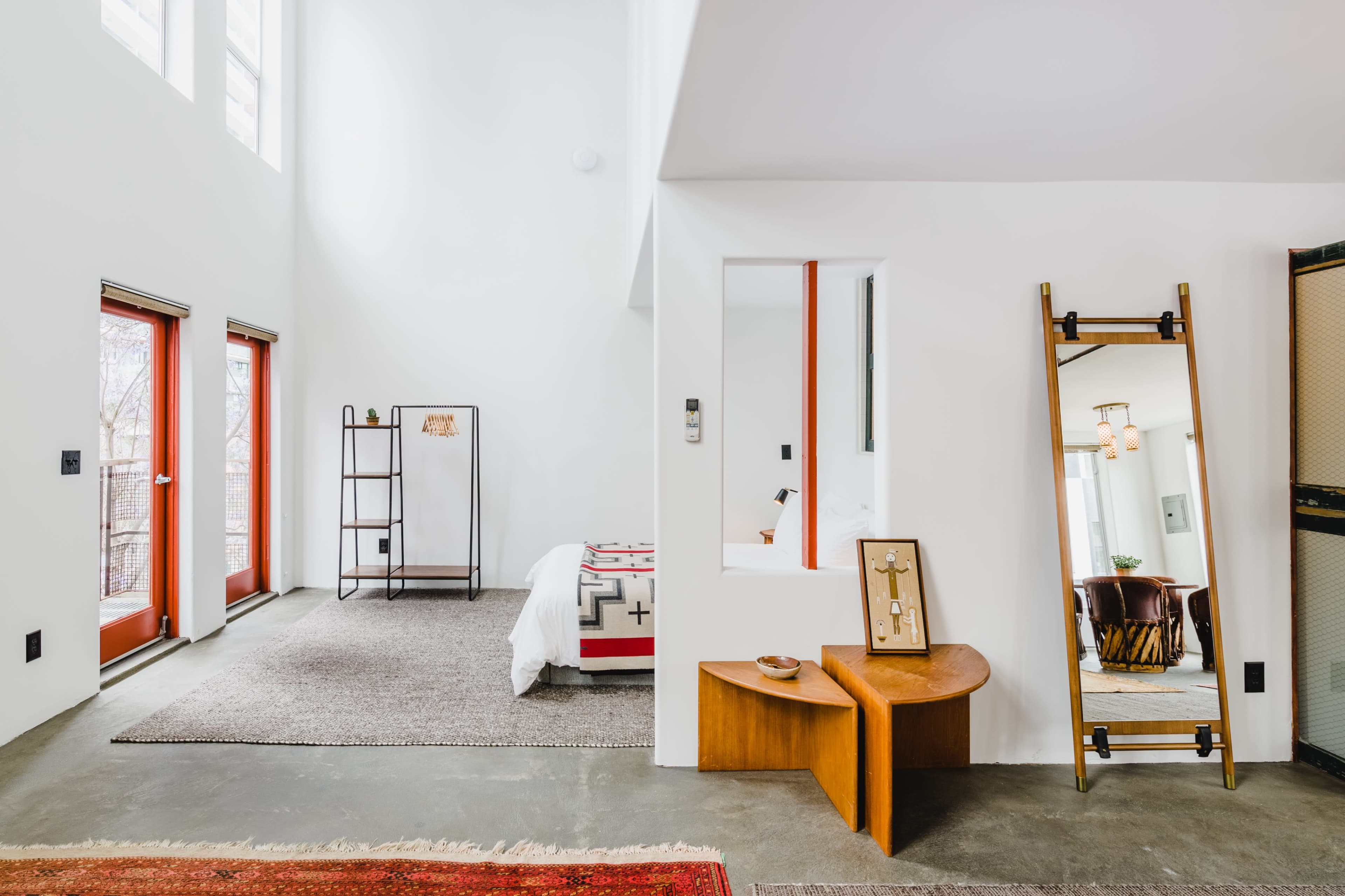 A modern interior features a bright room with large windows, a patterned rug, a minimalist wooden bench, and a decorative mirror.