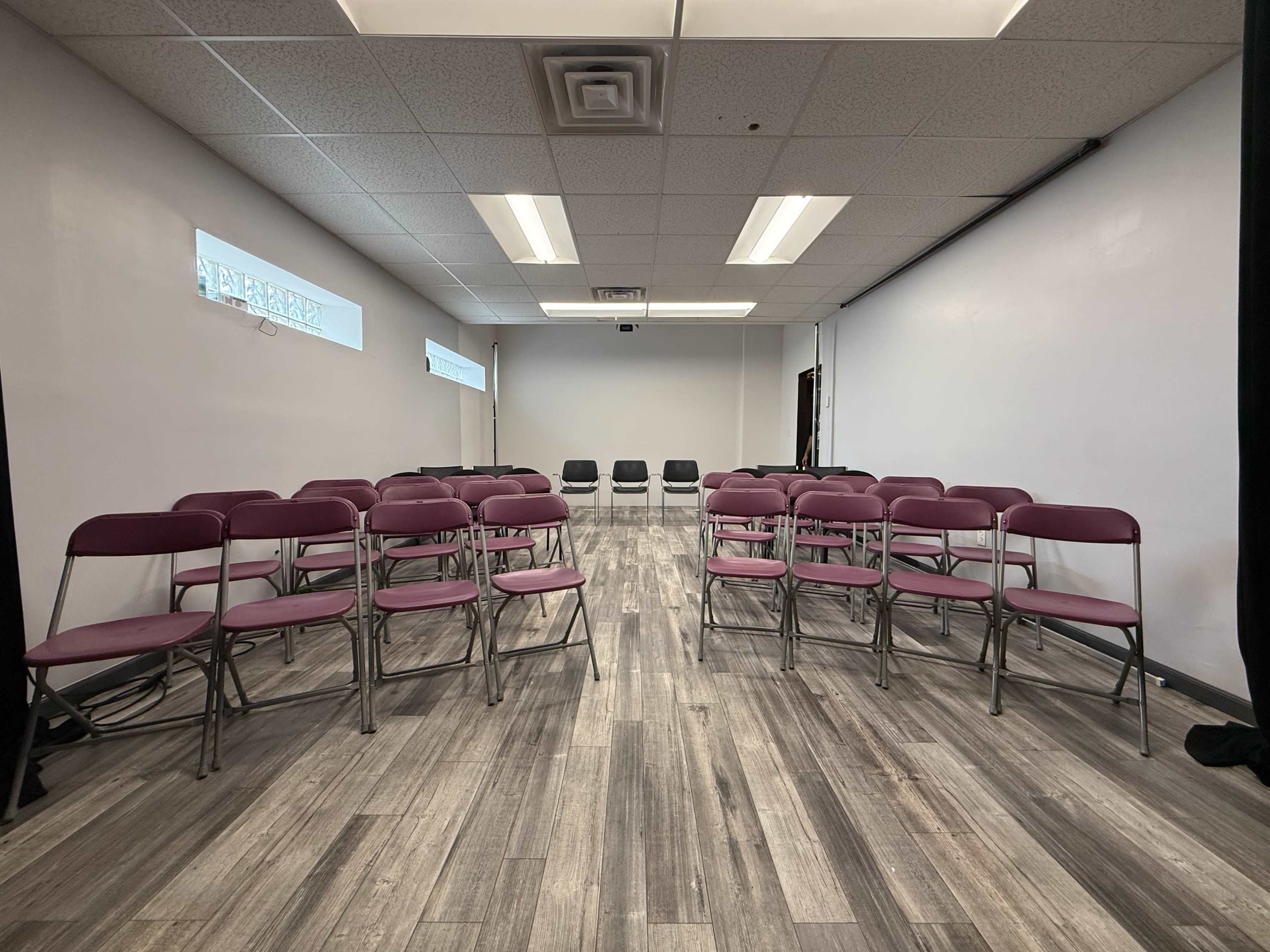 The image shows a spacious room with several rows of purple folding chairs arranged in a semi-circular formation on a wooden floor.