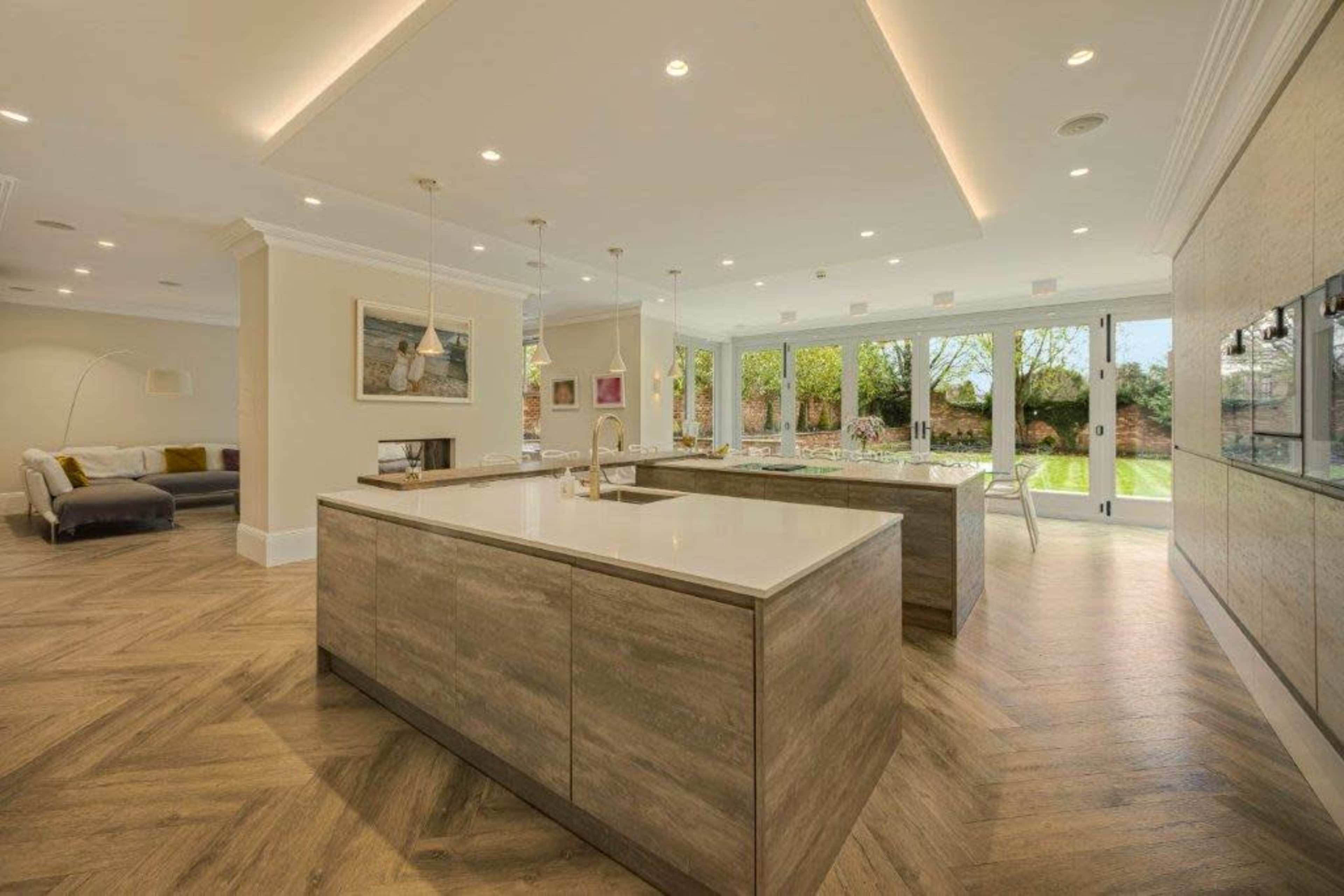 The image shows a modern kitchen with an island, wood flooring, and large glass doors leading to an outdoor area.
