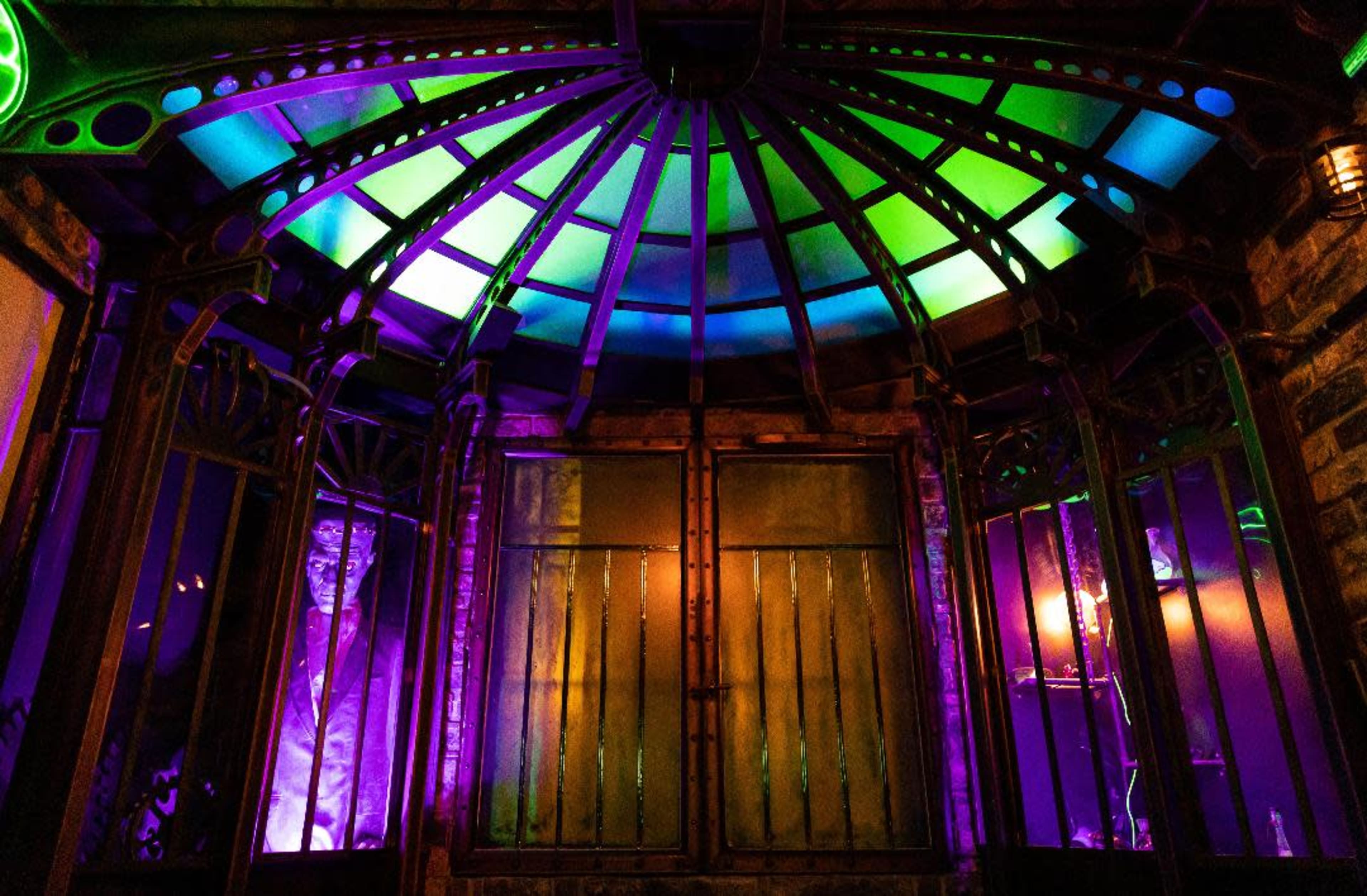A decorative entrance with a domed, multicolored ceiling and metal framing illuminated by purple and green lights.