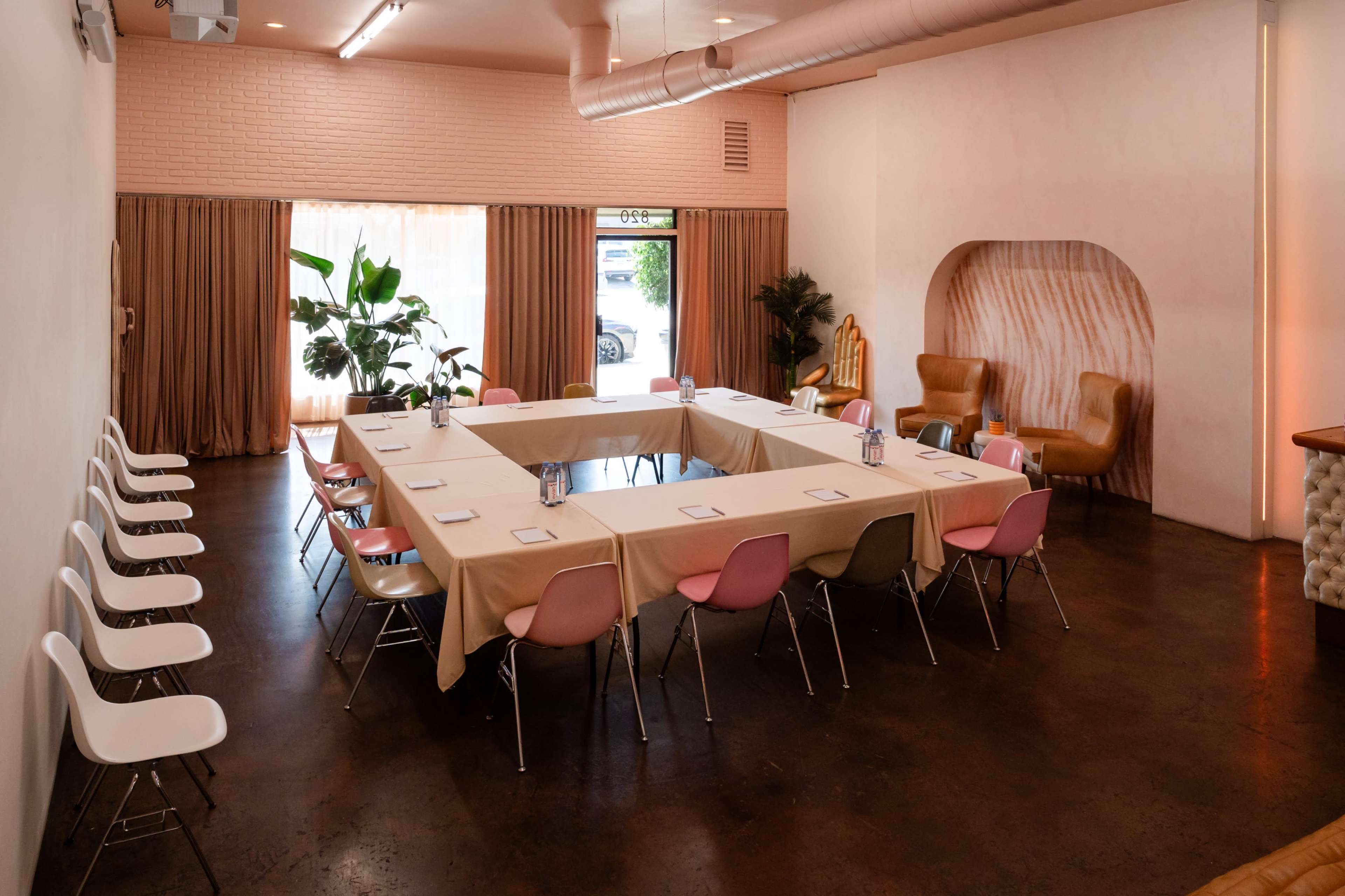 A spacious meeting room features a large, rectangular table surrounded by chairs, with natural light streaming in through large windows.