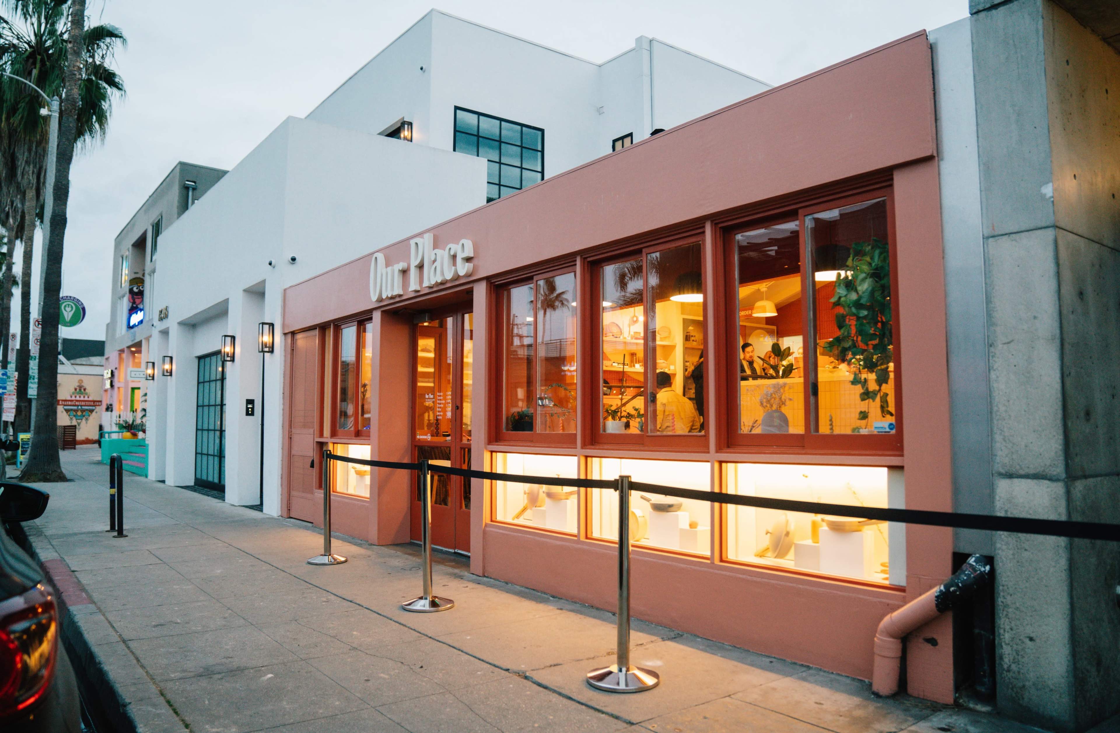 A modern storefront with large windows displaying a variety of kitchen items and a sign that reads "Our Place."