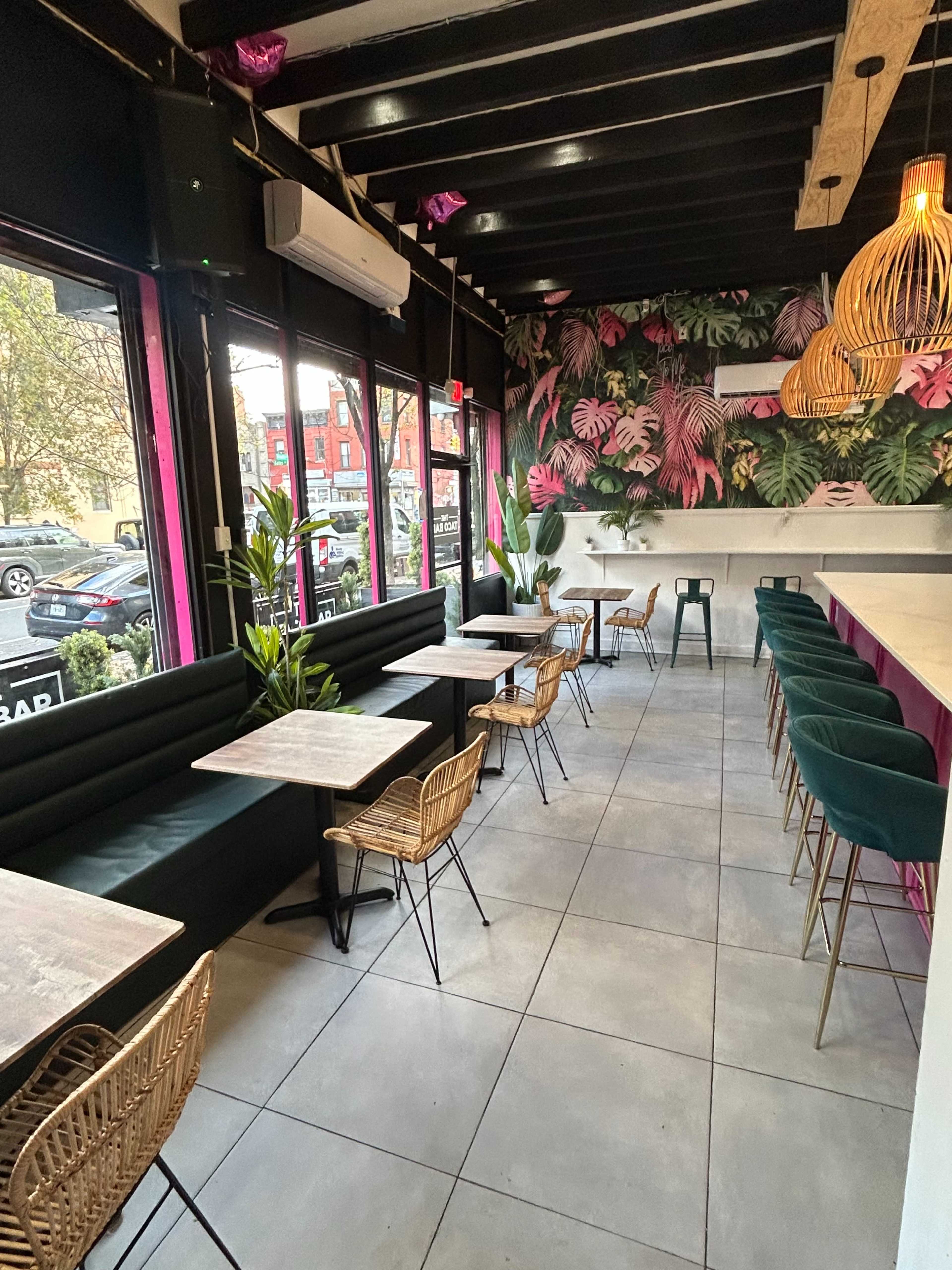 The image shows a modern restaurant interior with green seating, wooden tables, and a vibrant wall covered in tropical plant motifs.