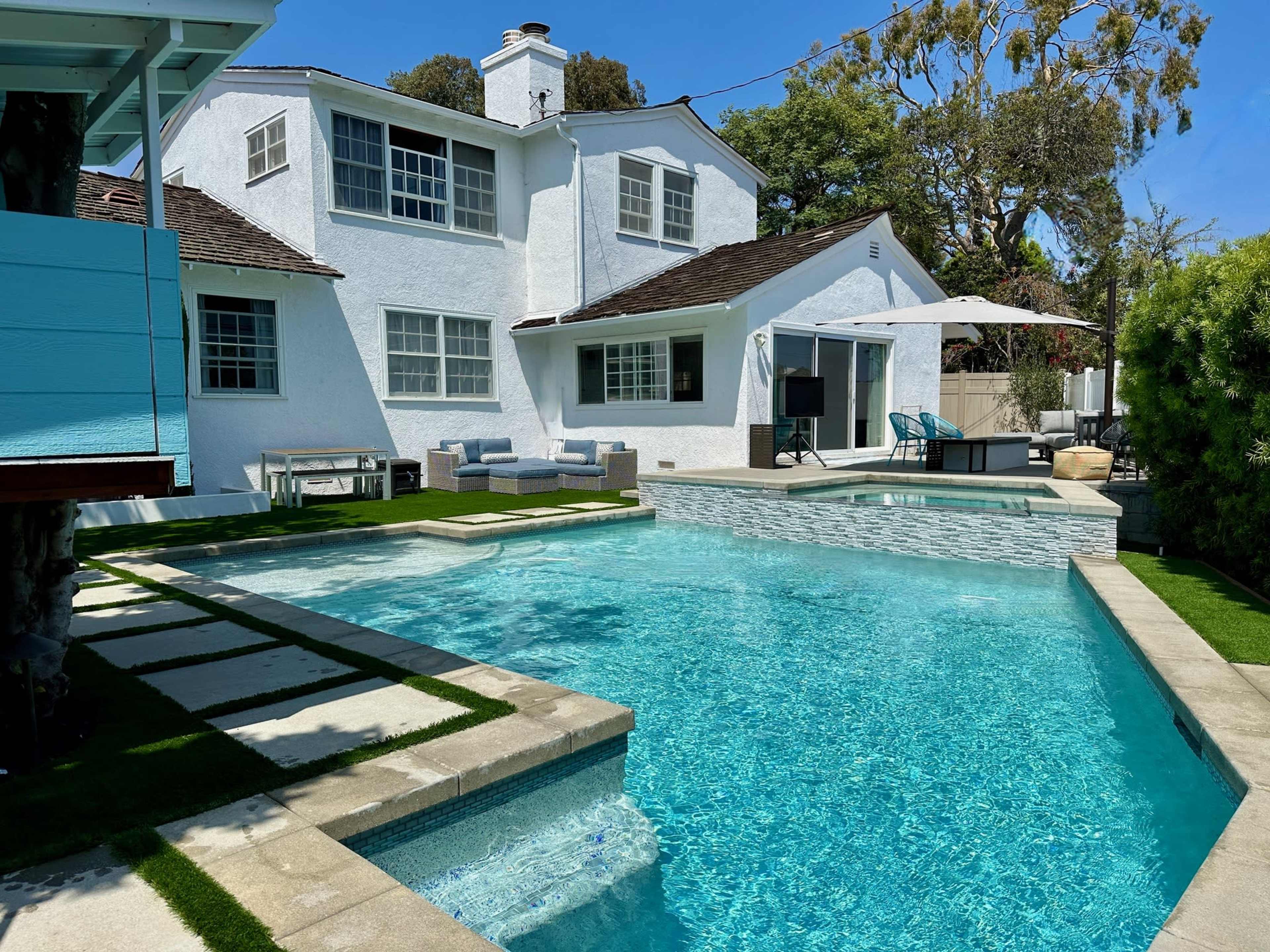 The image shows a modern residential backyard featuring a swimming pool, patio furniture, and a well-maintained lawn.