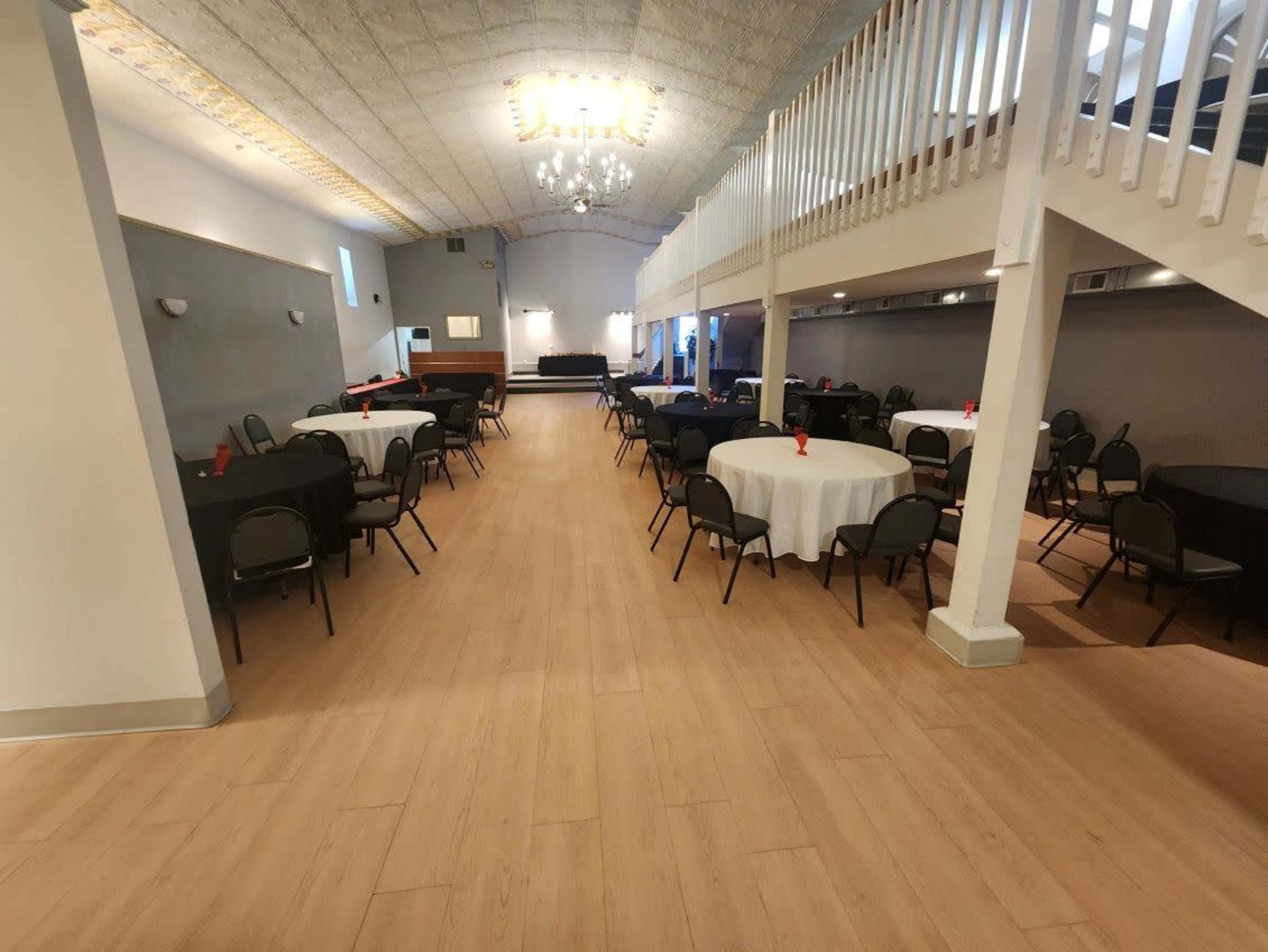 The image shows a spacious event hall with circular tables set for seating and a stage area in the background.