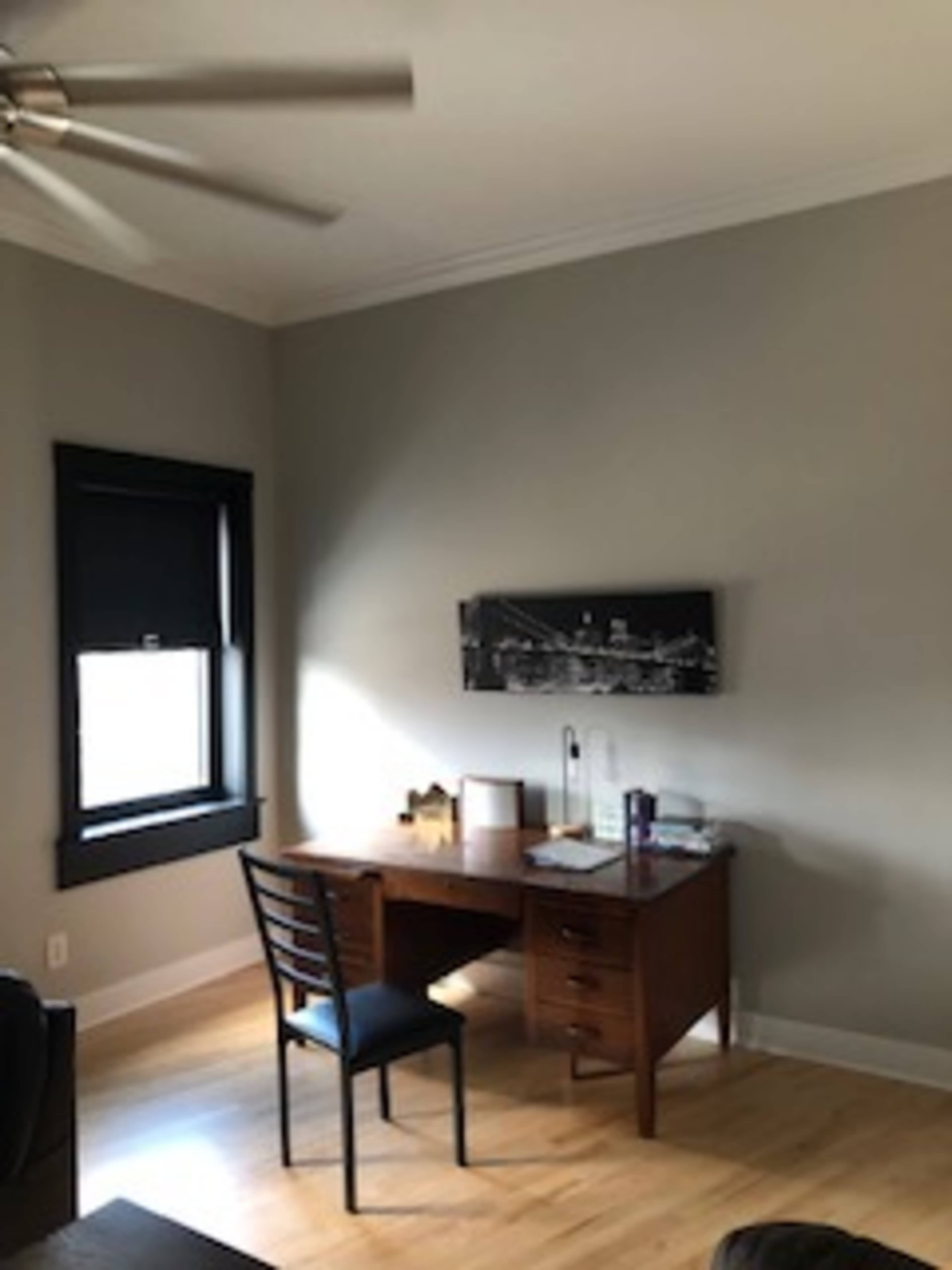 A simple home office with a wooden desk, a black chair, and a mounted black-and-white cityscape photo on the wall.