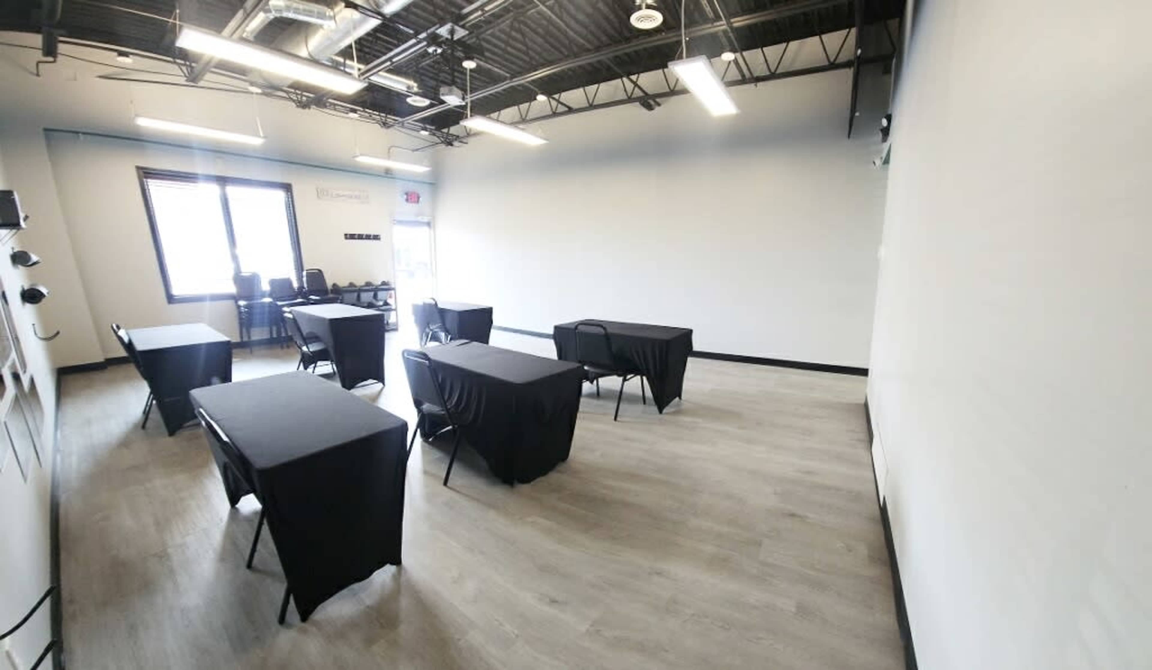 A spacious room features several tables covered with black tablecloths arranged in a layout on a light-colored floor.