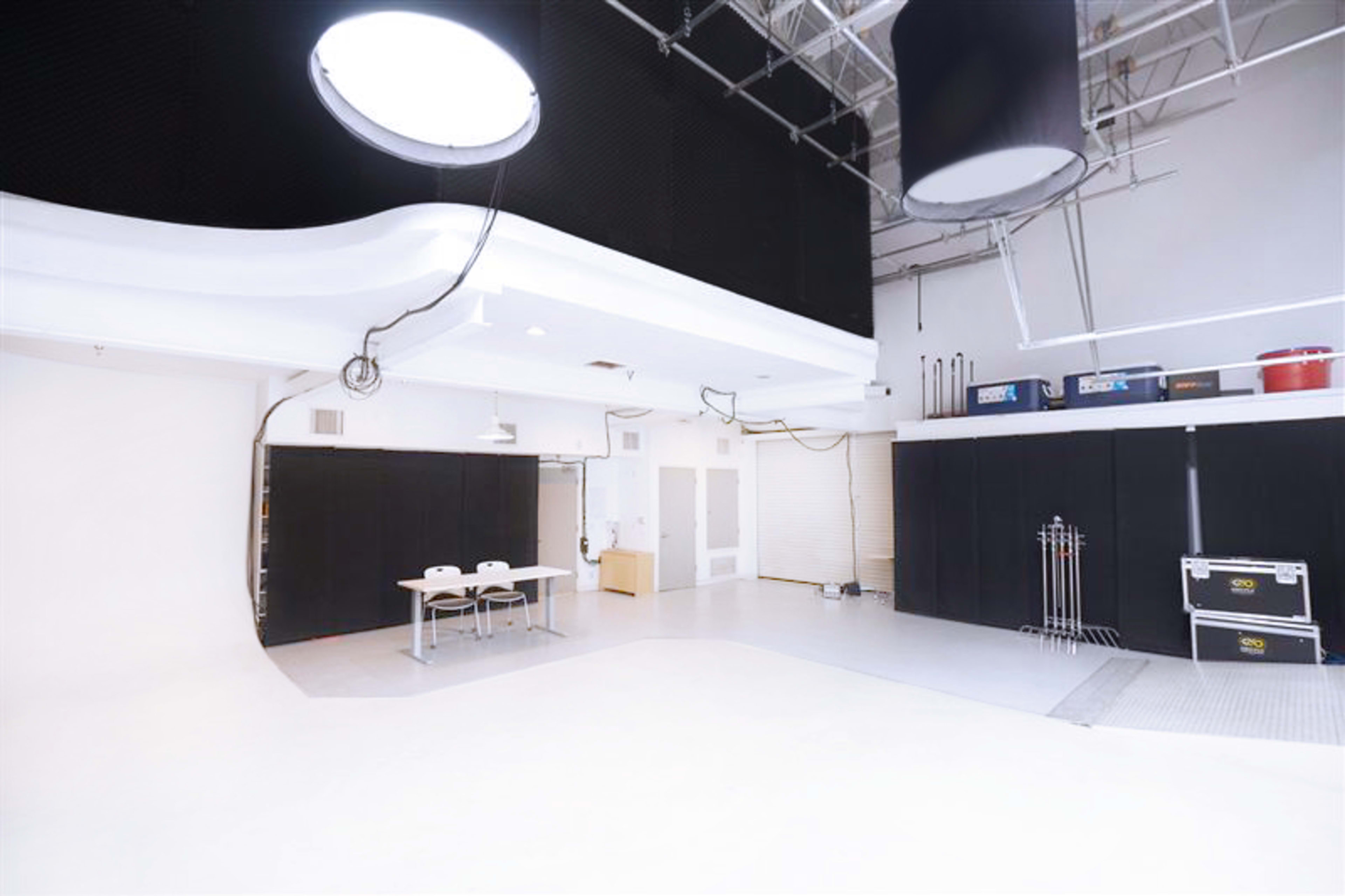 A spacious photography studio with white walls, a lighted ceiling, and a table set up in the center.