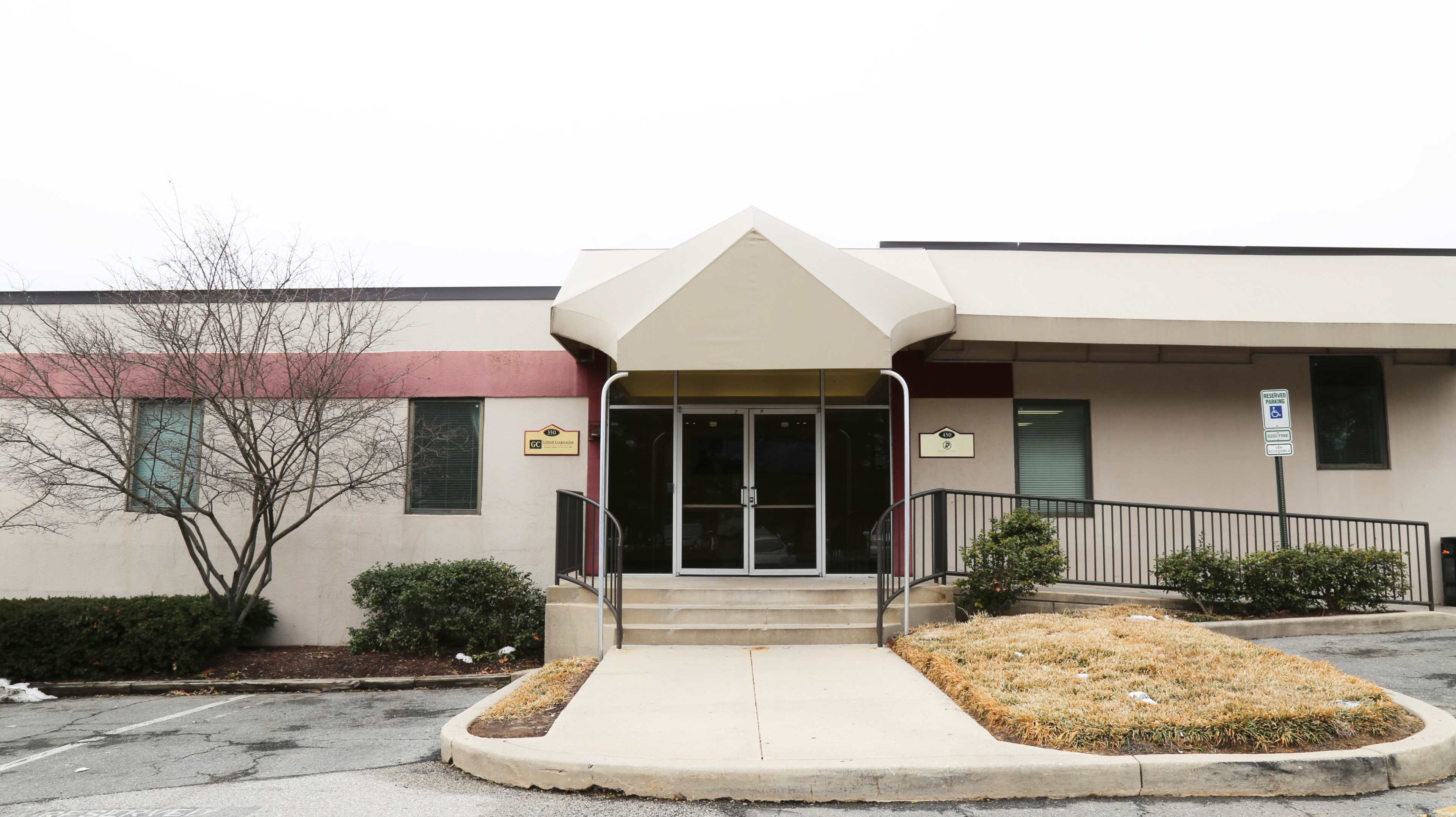 The entrance of a single-story building with a canopy over the door and landscaped shrubs on either side.