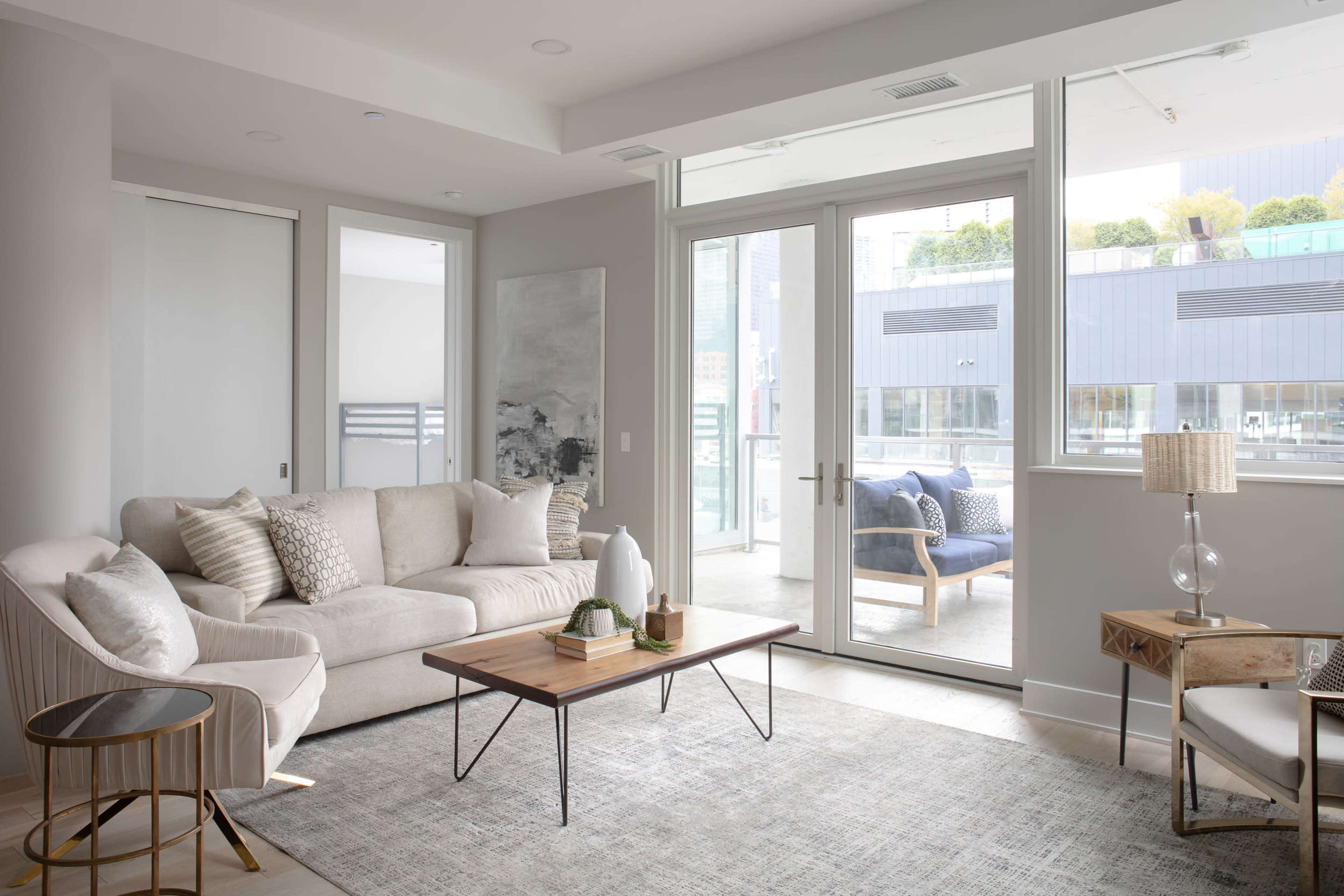 A modern living room with a light-colored sofa, a wooden coffee table, and large windows that provide ample natural light.