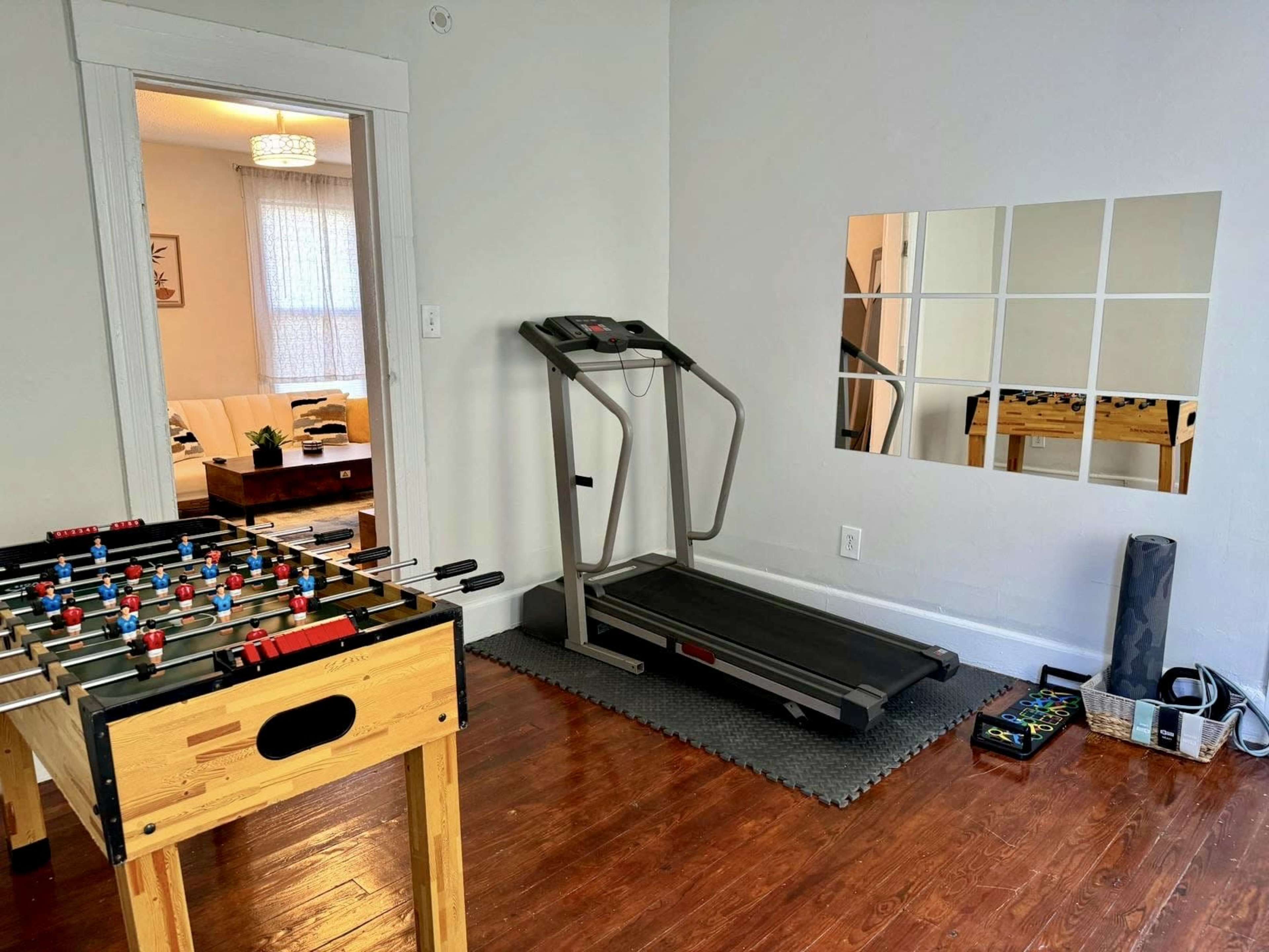 A room featuring a foosball table, a treadmill, and a mirrored wall in a minimalist space.