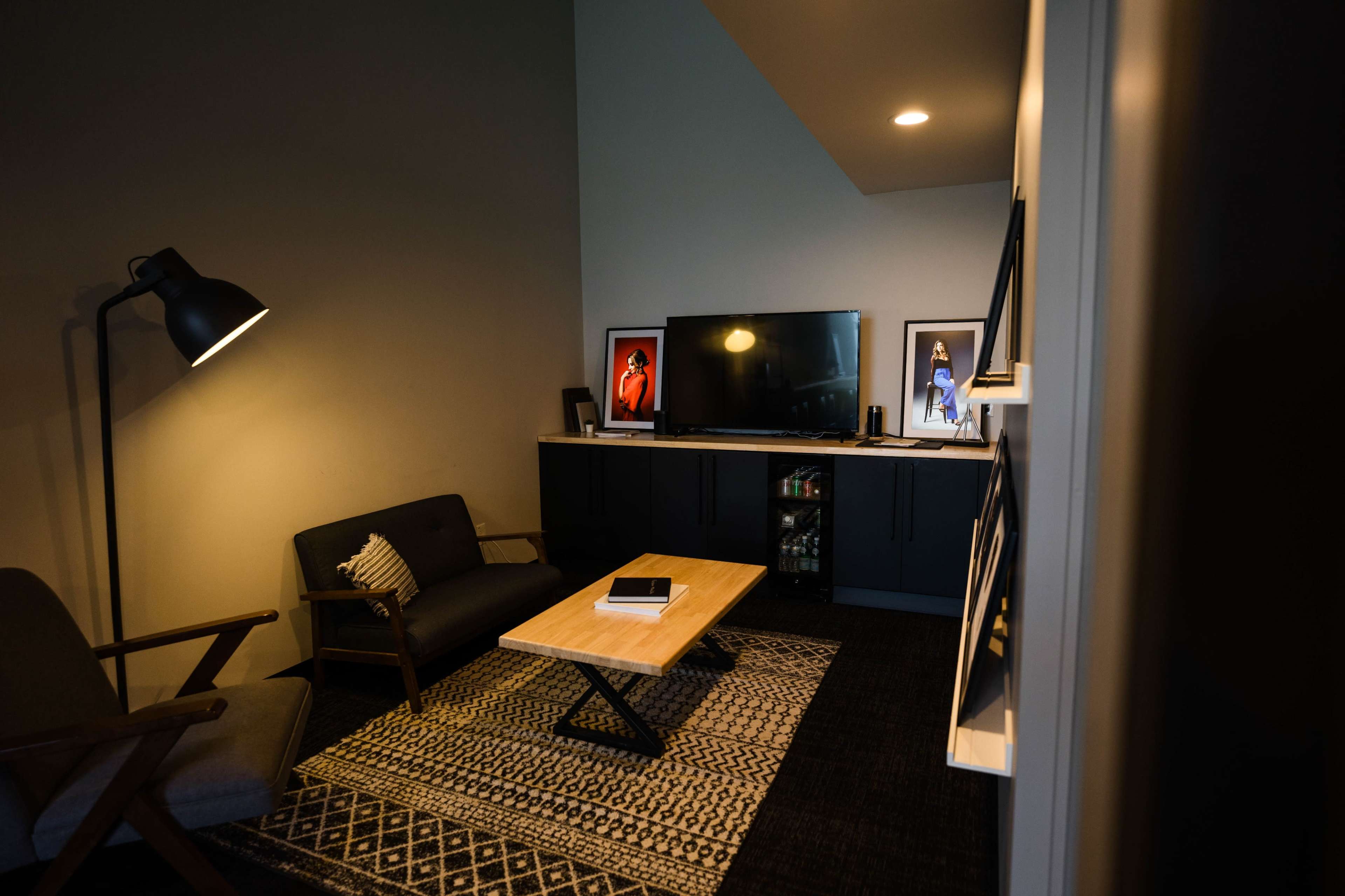 A small, modern living room featuring a television, a wooden coffee table, two seating areas, and framed artwork on the walls.