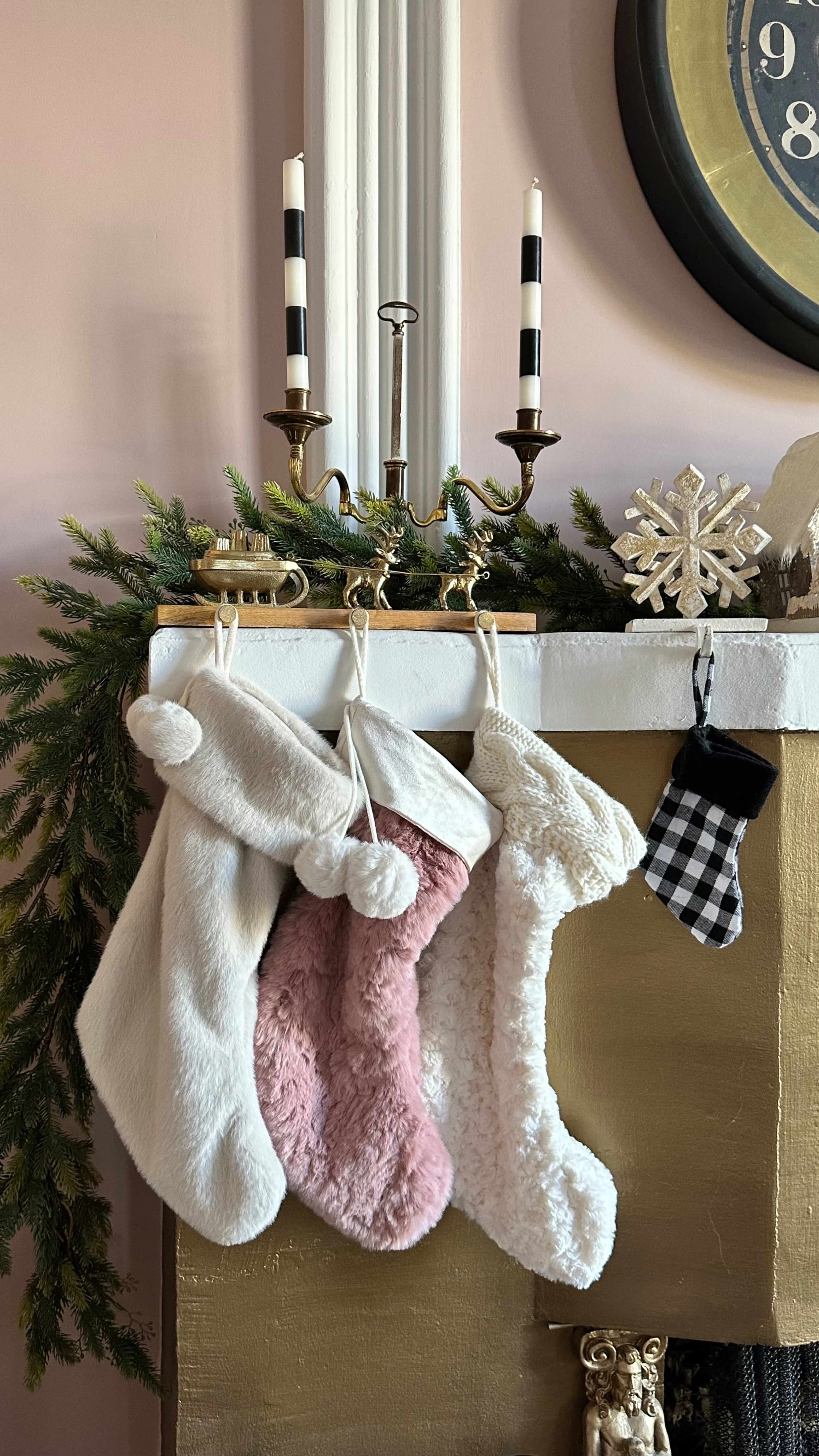 The image shows a decorated mantel with various Christmas stockings hanging, flanked by candles and a snowflake ornament.