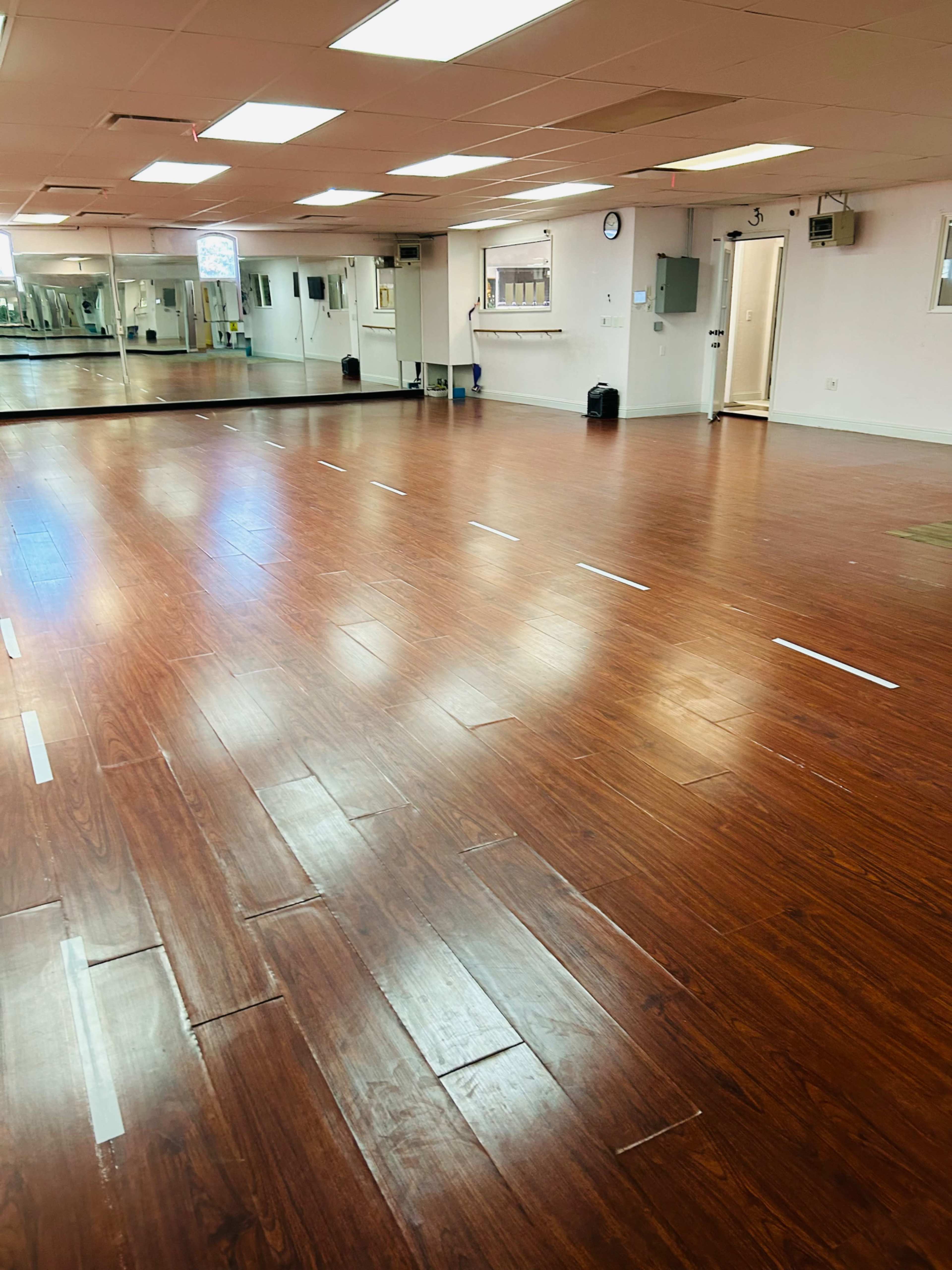 A spacious dance studio with a polished wooden floor and large mirrors along one wall.