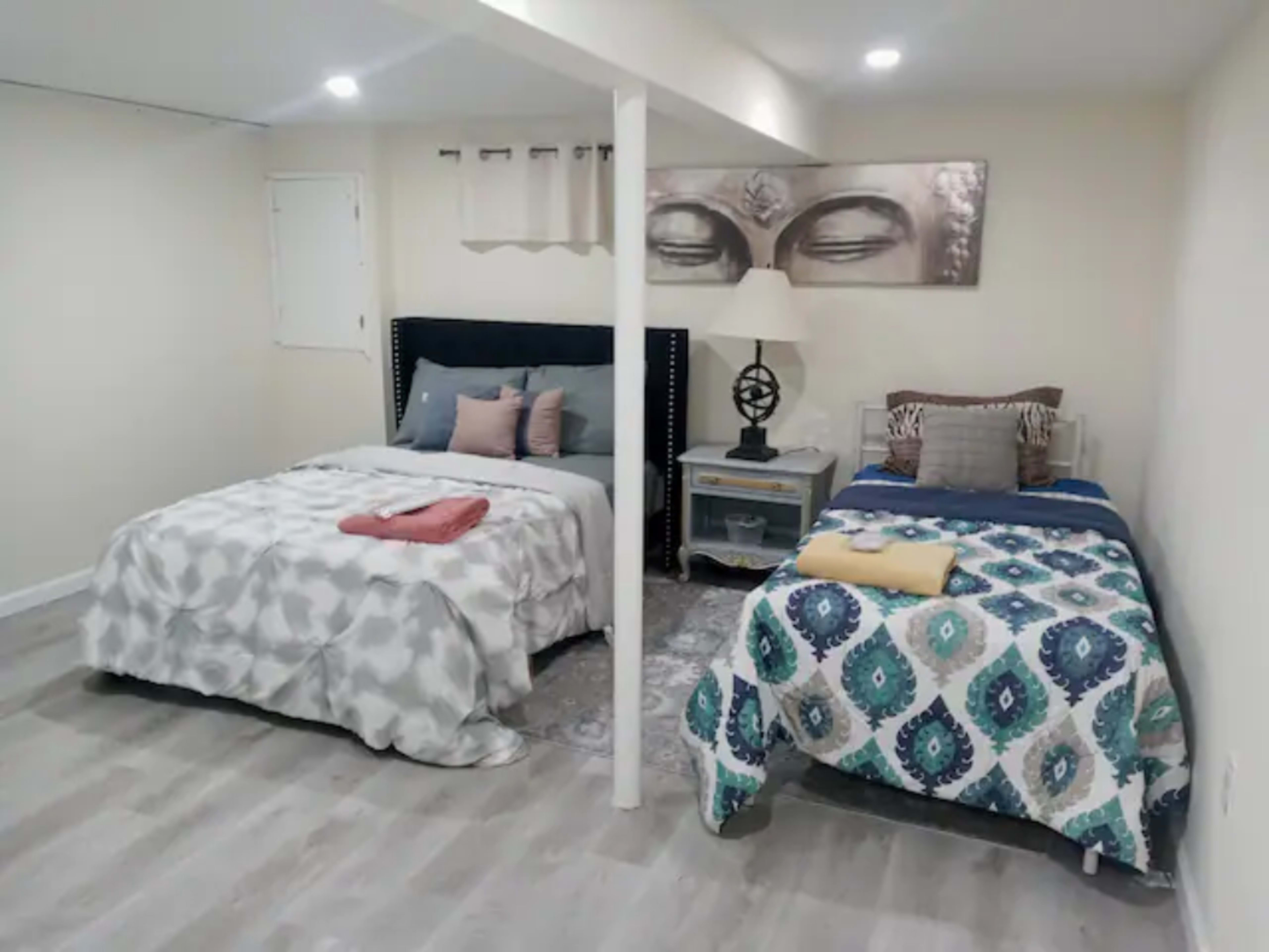 A spacious bedroom with two beds, a nightstand, and wall art featuring a large face above the beds.