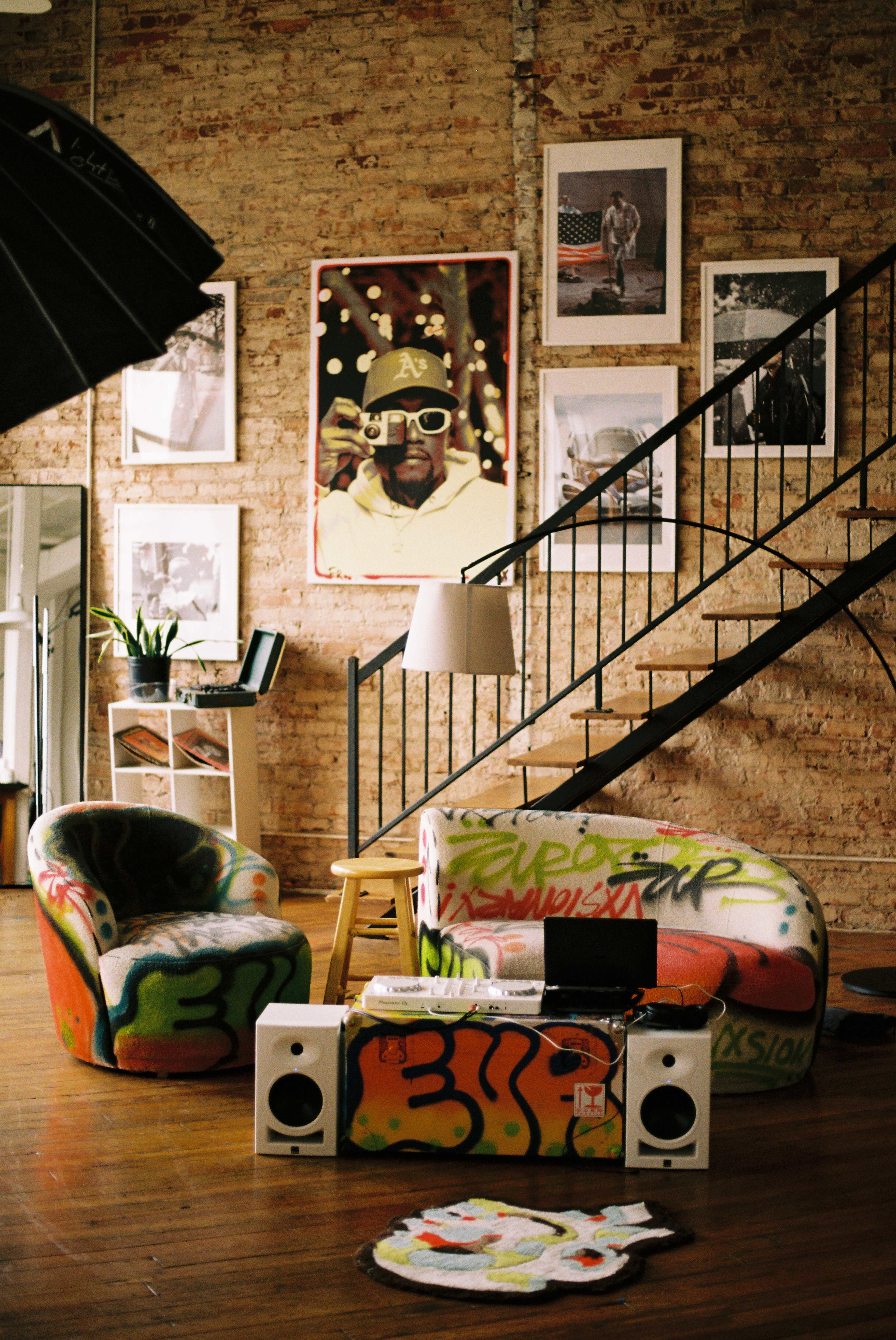 The image displays a creatively decorated interior with colorful, graffiti-style furniture, framed artwork on the walls, and a staircase in the background.