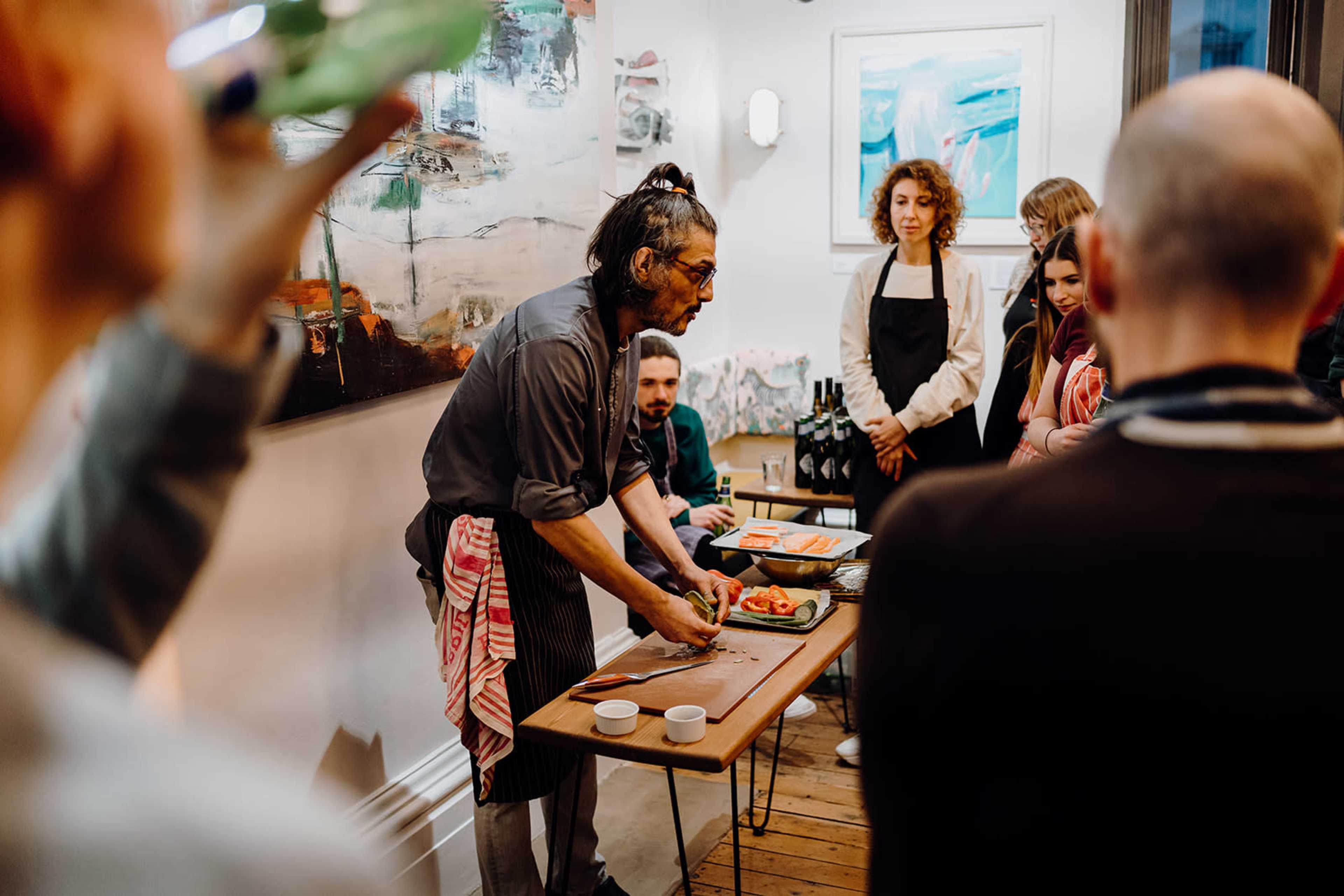 A chef demonstrates food preparation techniques to an attentive audience in a vibrant kitchen setting.