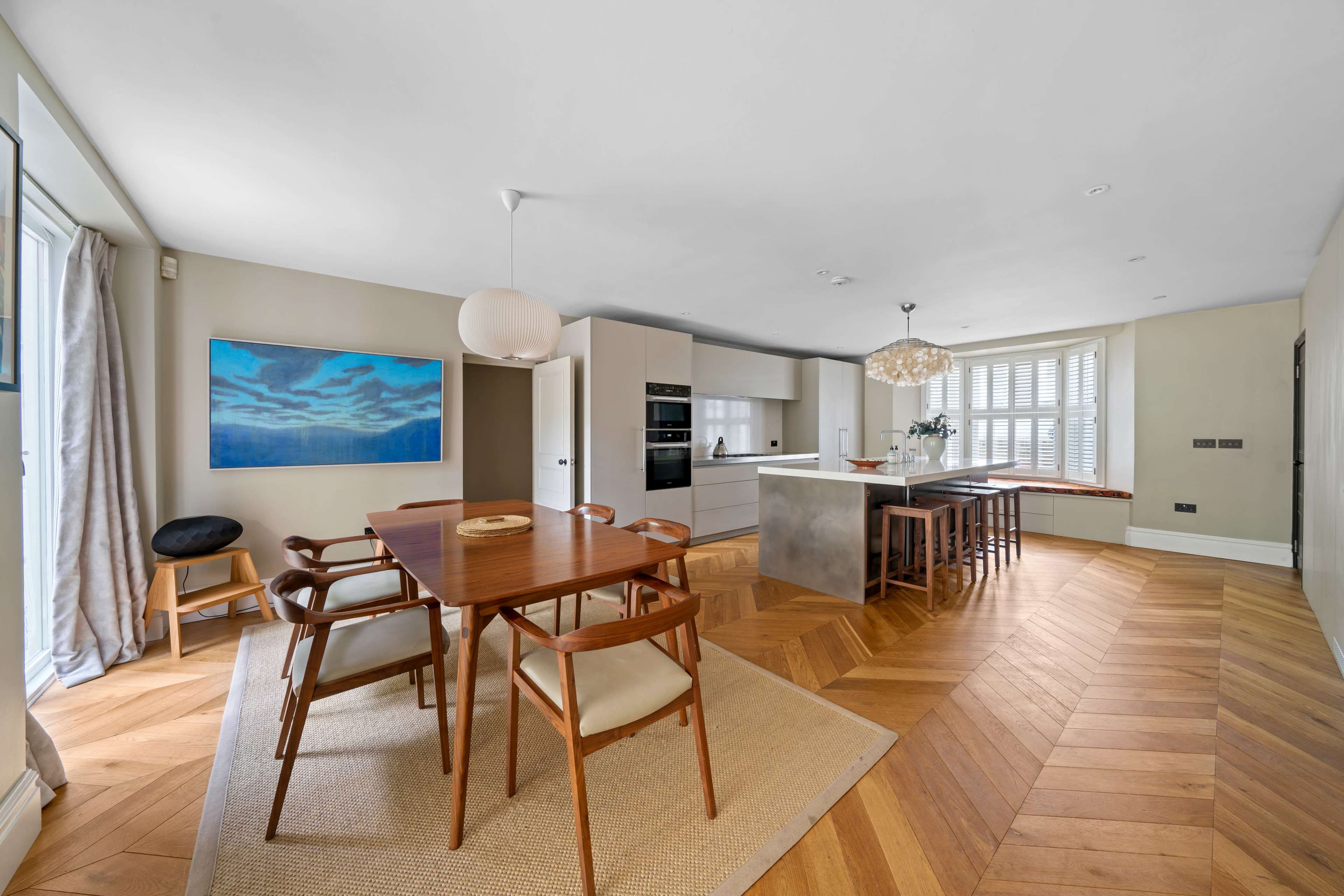 A modern open-concept kitchen and dining area features a wooden dining table with chairs, a large island, and large windows letting in natural light.
