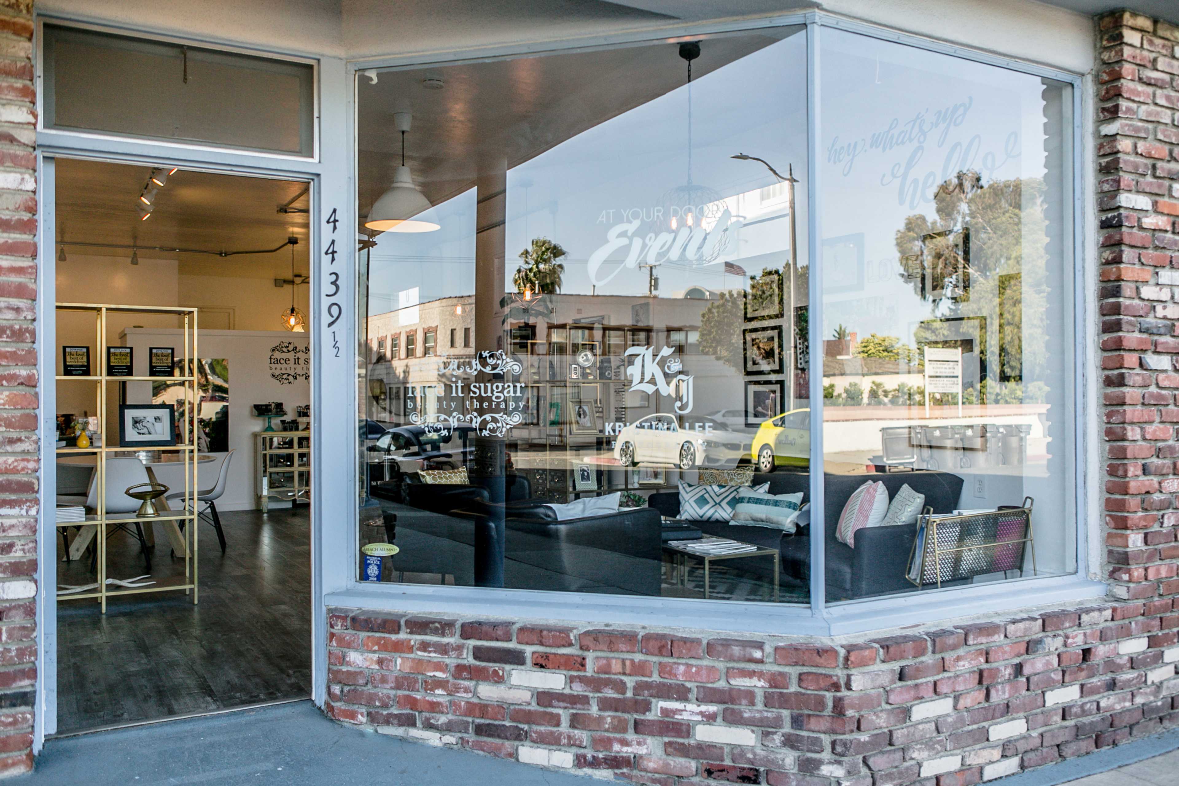 A storefront with large windows displays a welcoming interior featuring decorative items and furniture.
