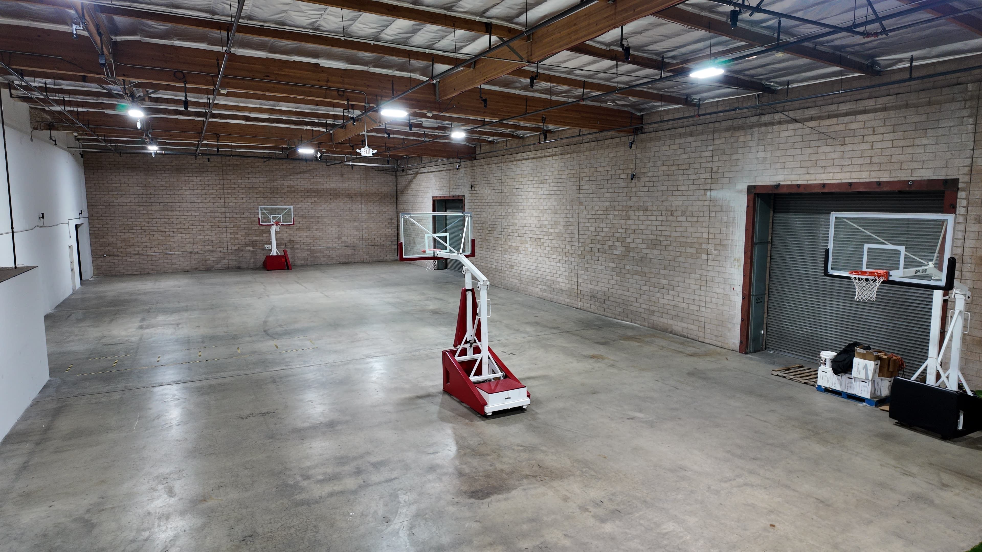 The image shows a large, empty indoor basketball court with two hoops positioned on opposite ends.