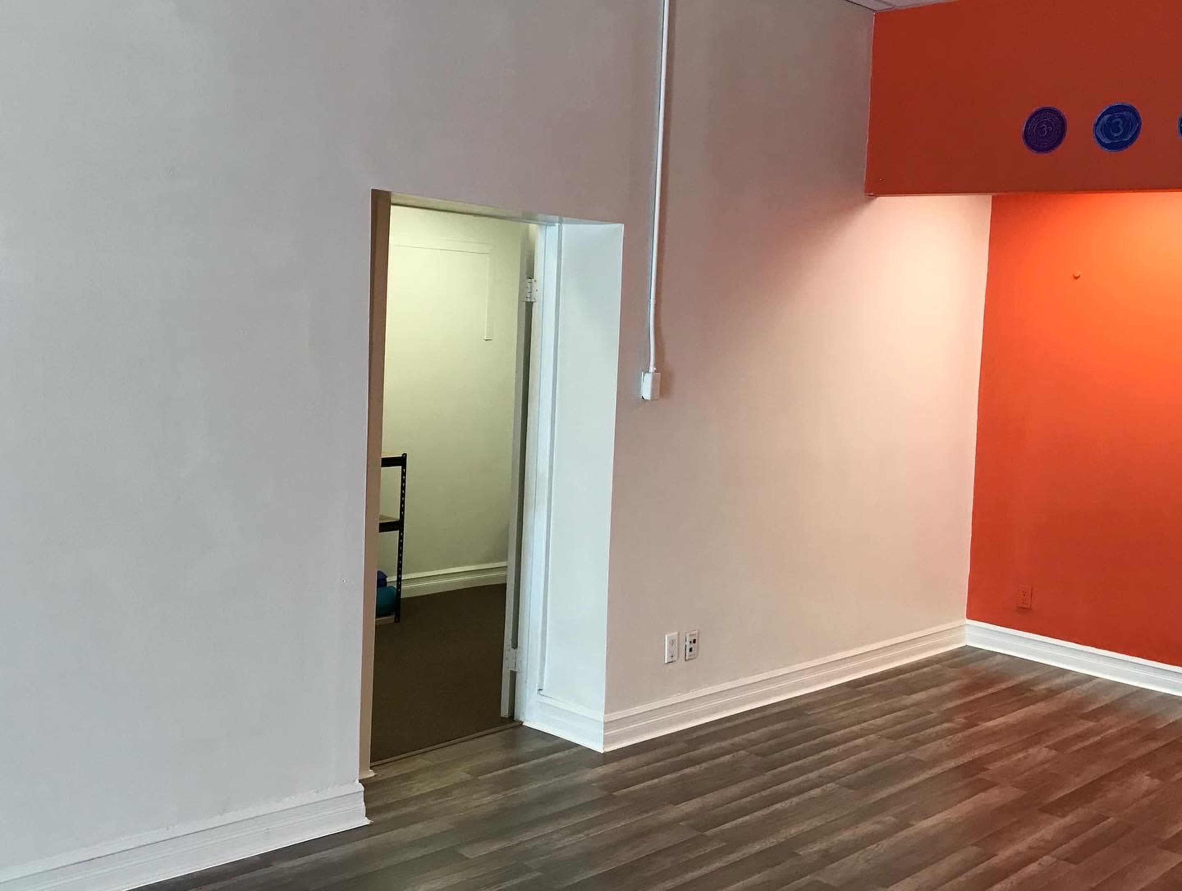 A room with a wood floor and a partially open doorway leading to another room, featuring an orange accent wall.