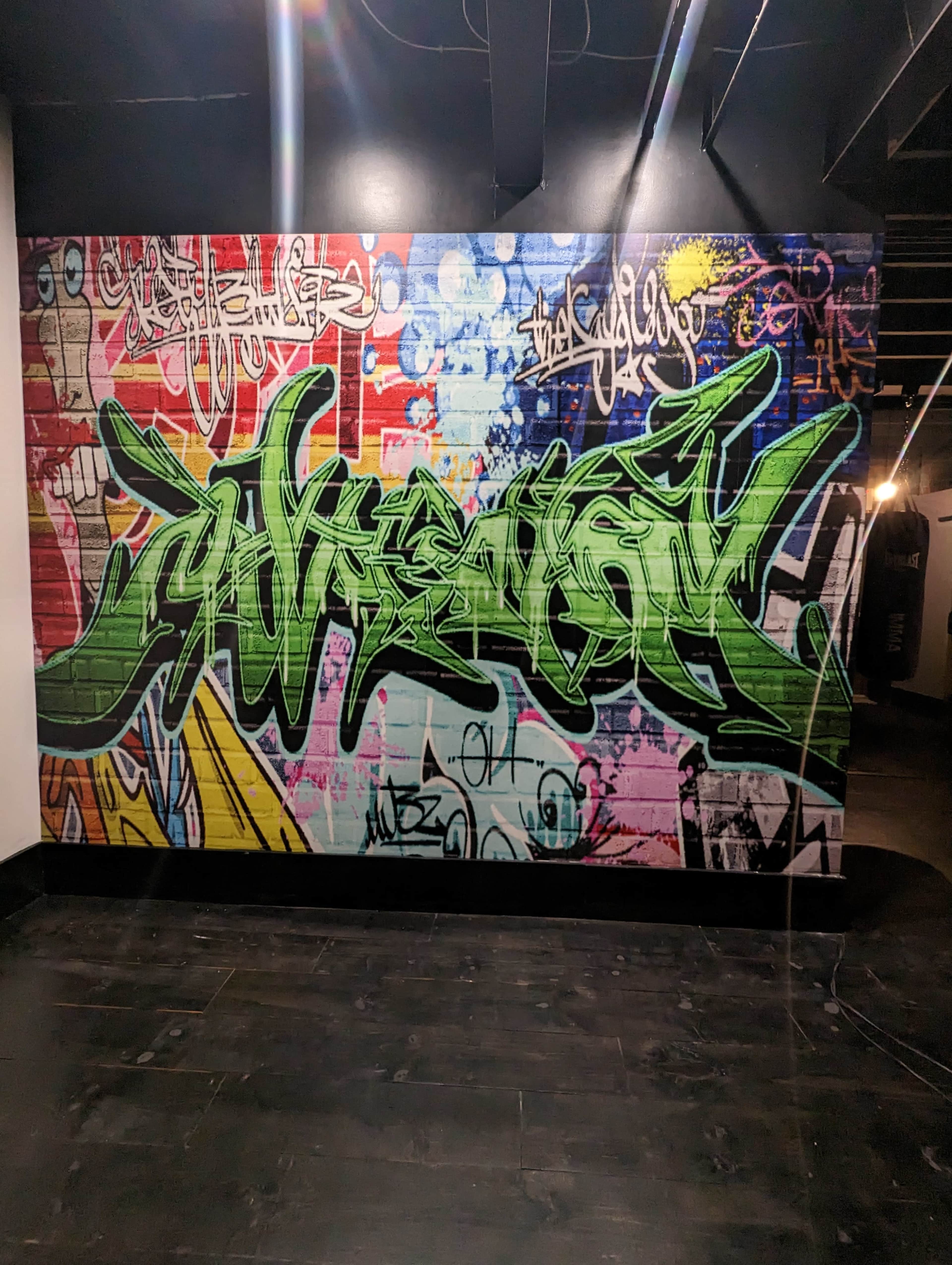 A large graffiti mural with vibrant green lettering and colorful background patterns on a brick wall.
