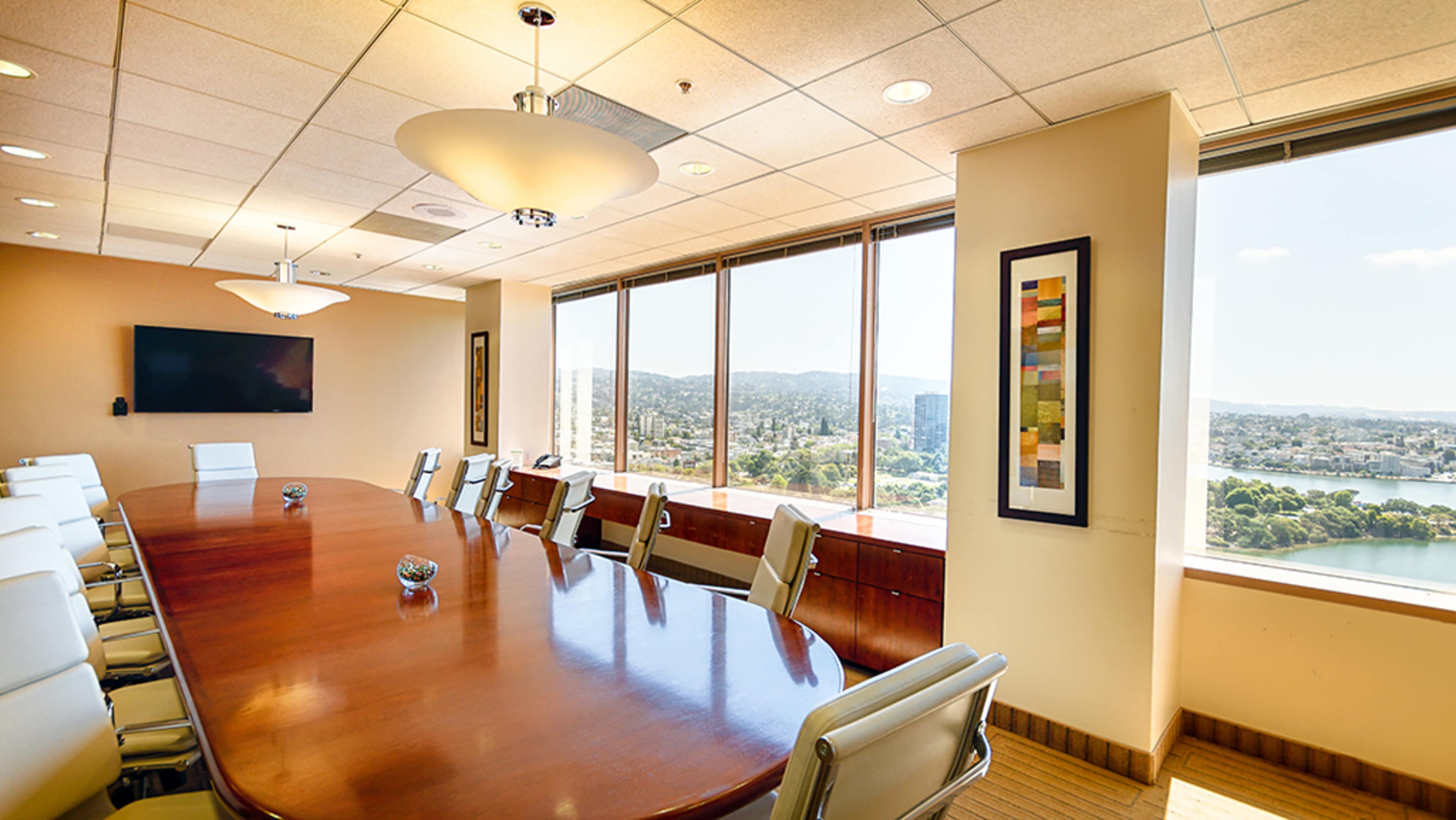 A large conference room features a wooden table surrounded by white chairs, with large windows offering a view of the cityscape.