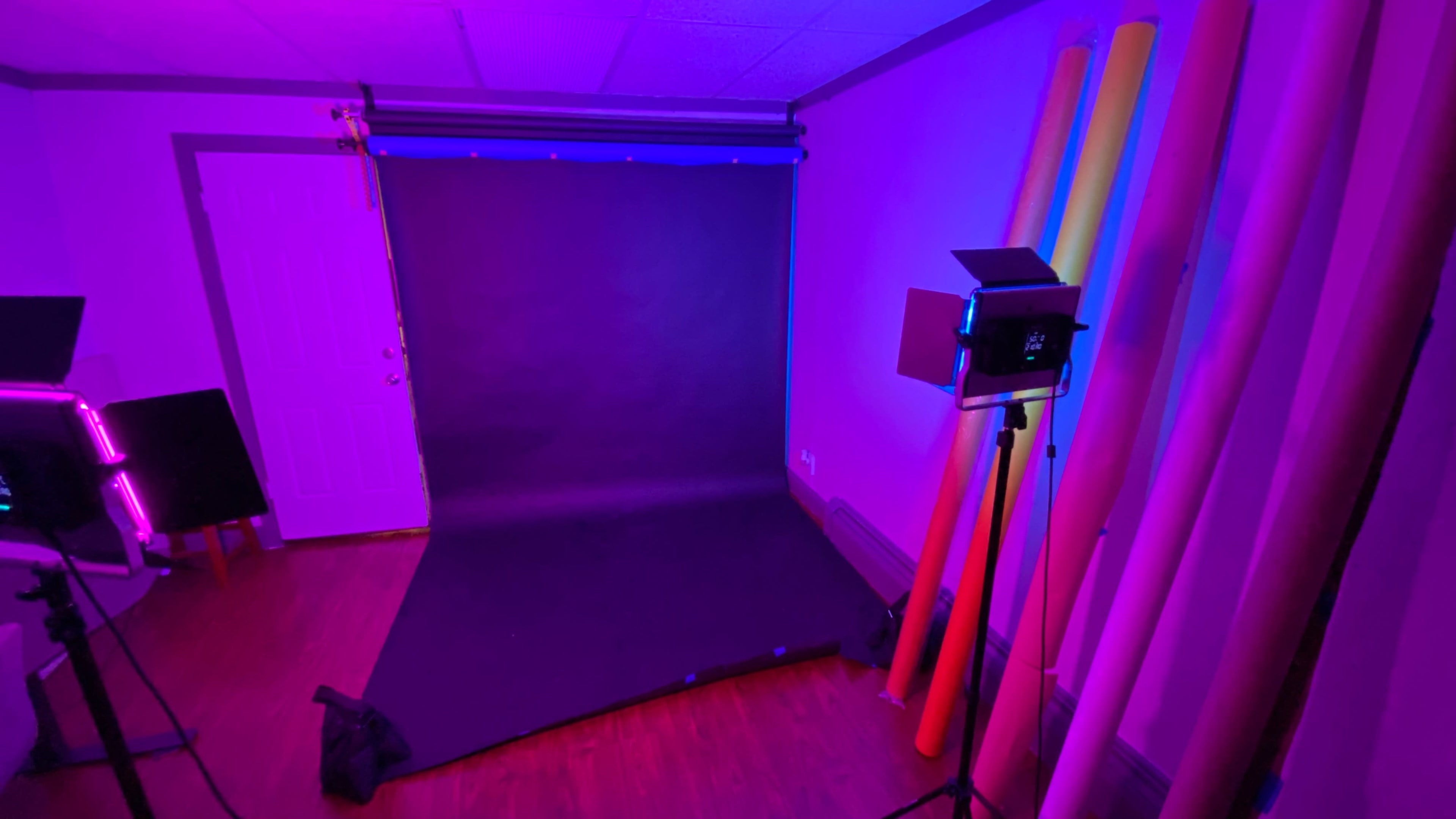A photo studio with a dark backdrop, a light stand, and colorful backdrop rolls leaning against the wall.
