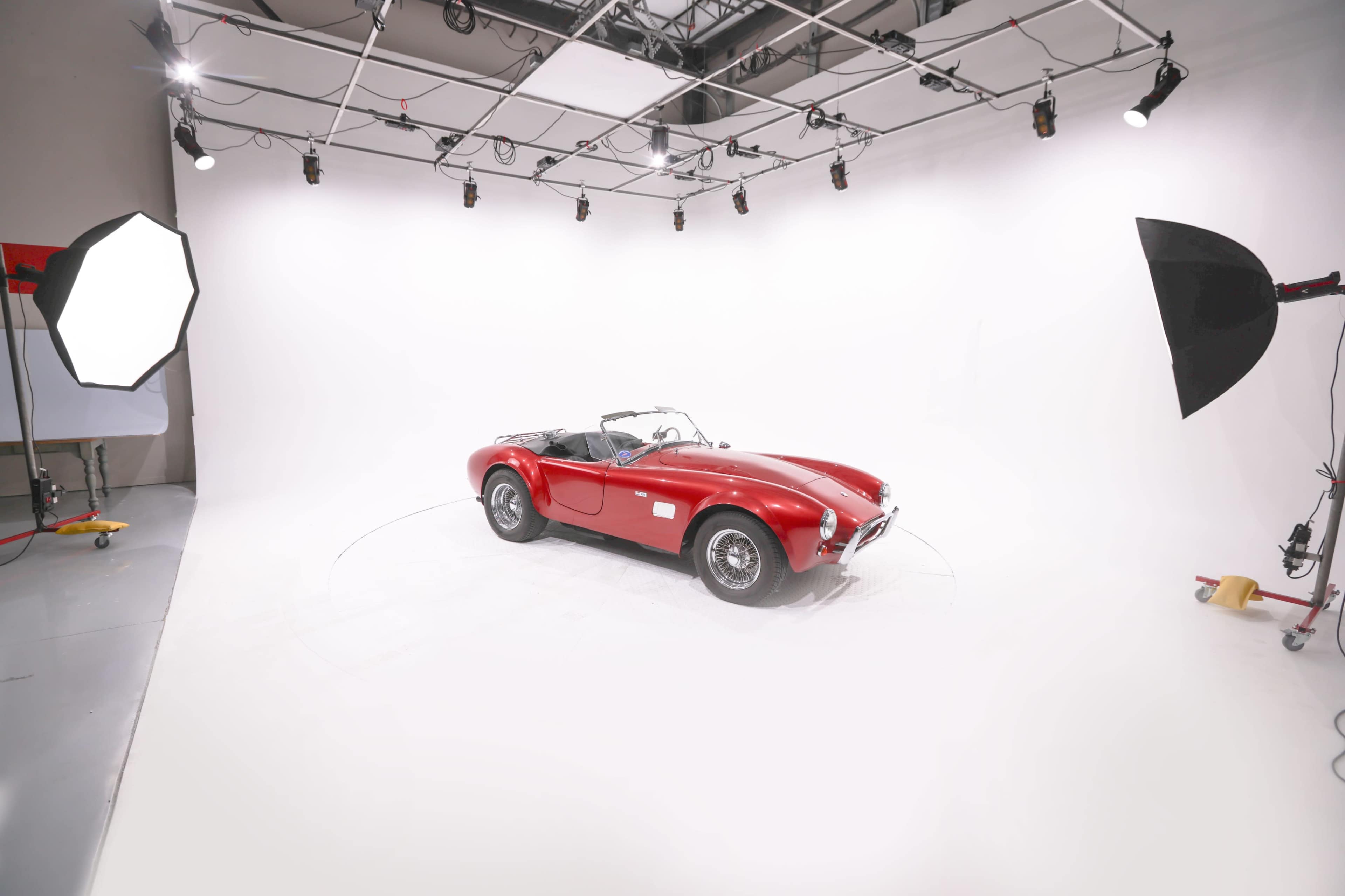 A red classic convertible car is displayed in a brightly lit studio with a white backdrop.