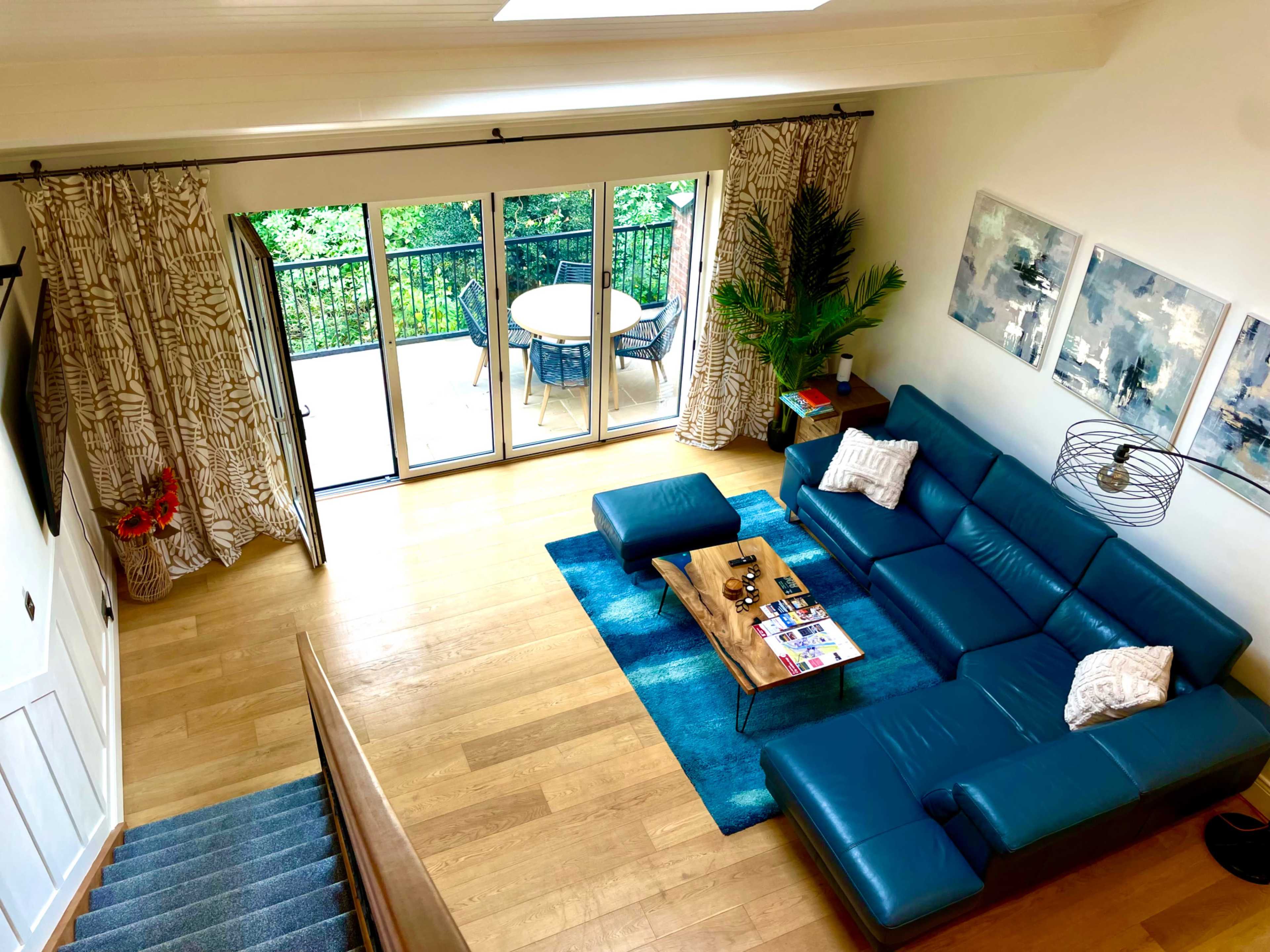 The image shows a spacious living room featuring a large blue sectional sofa, a coffee table with magazines, and a view of an outdoor balcony through sliding glass doors.